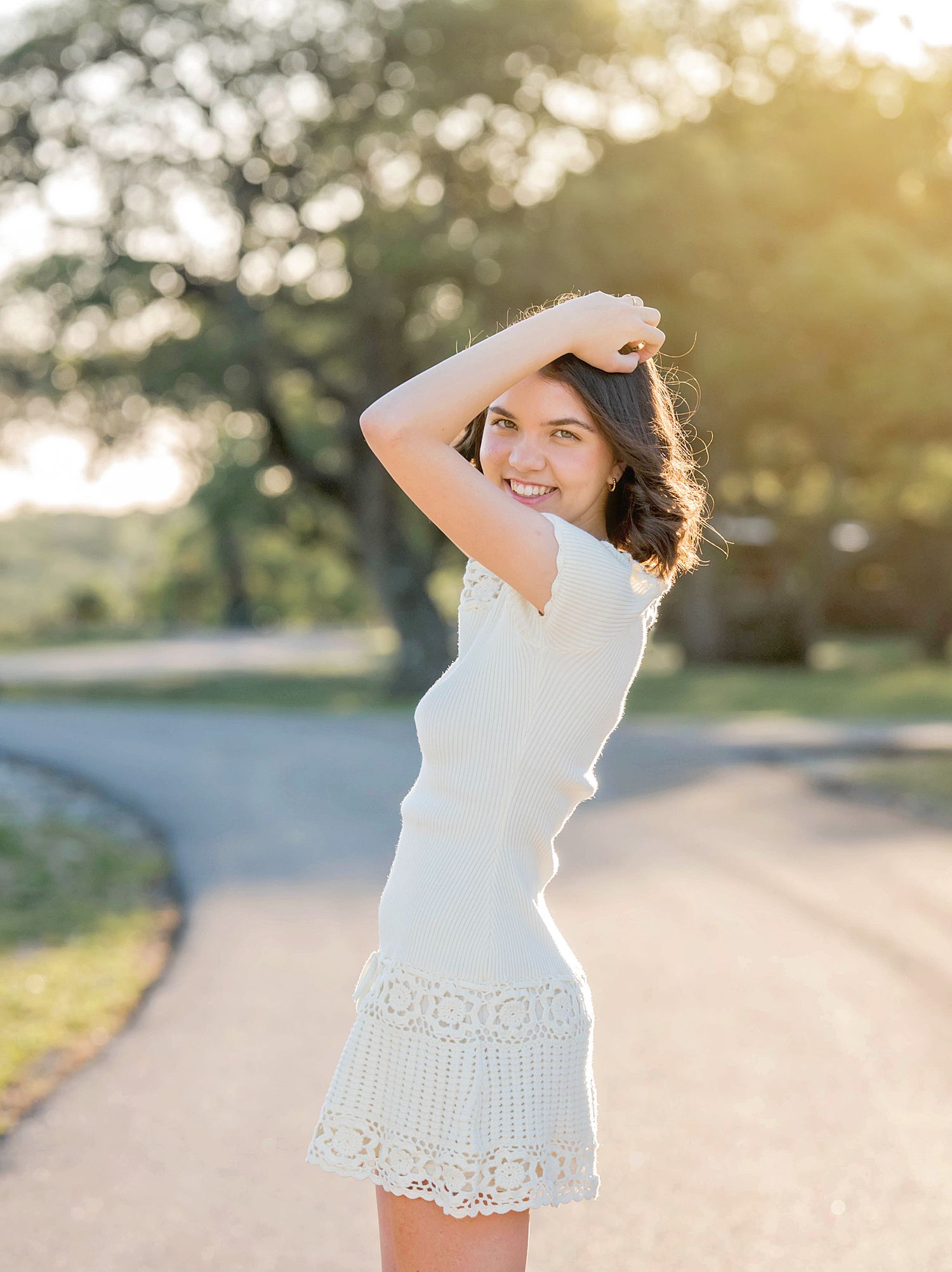 A dreamy outdoor portrait showing someone in a white lace dress with sunlit trees bokeh in the background.