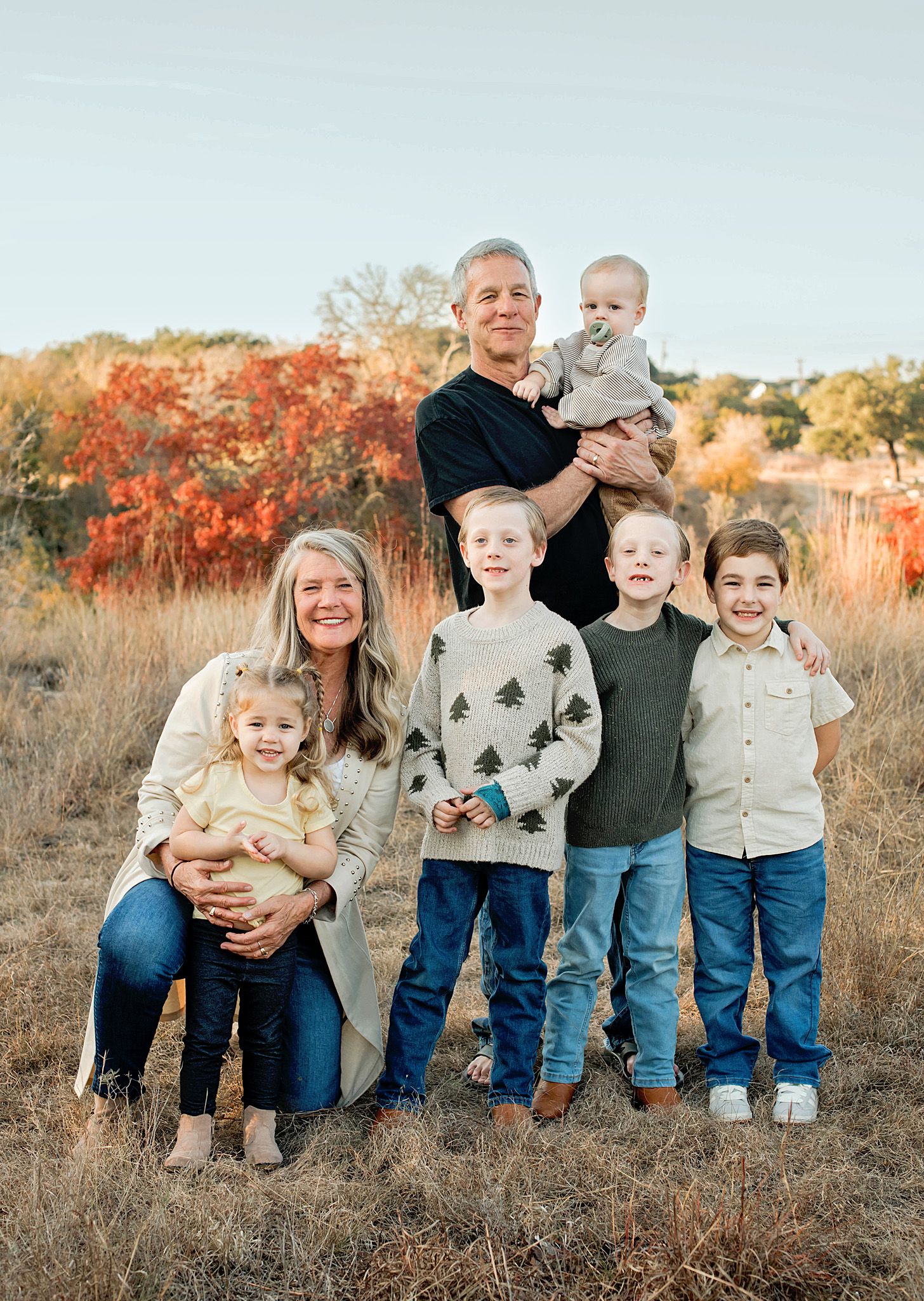 Family of seven posing outdoors in a golden field with colorful autumn foliage in the background.