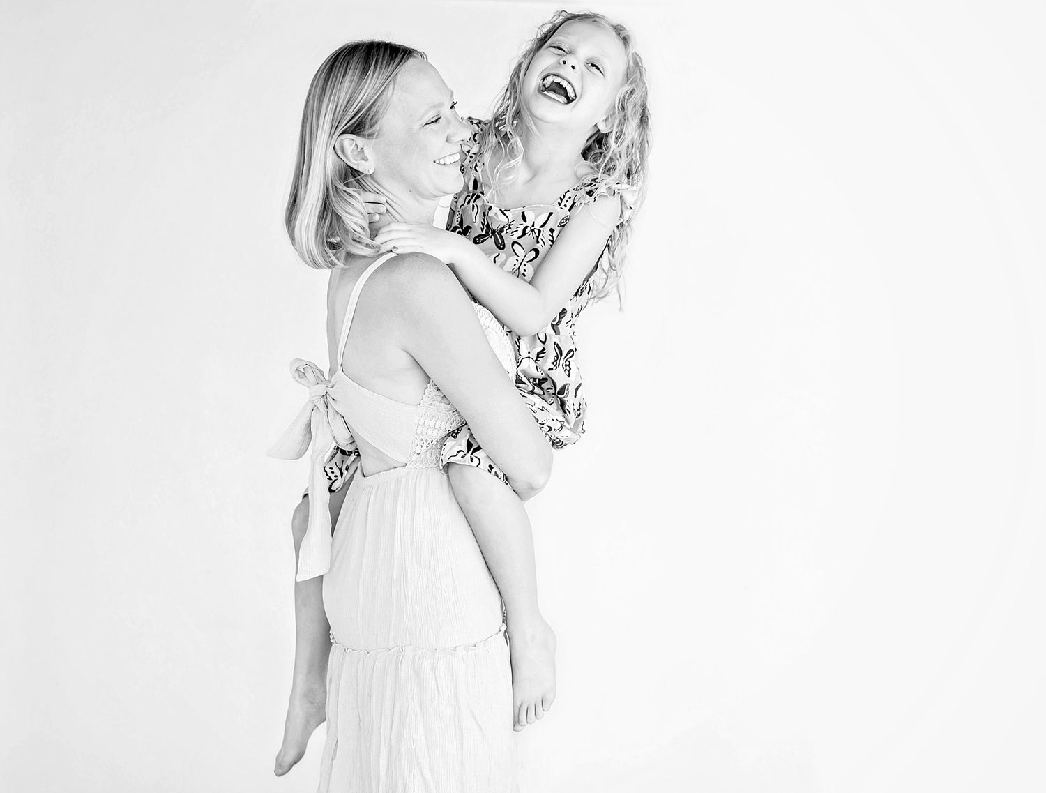 Black and white photo of a woman carrying a laughing young girl on her back, both smiling joyfully.