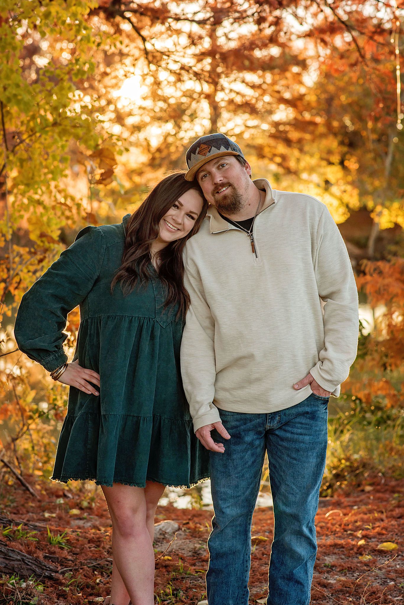 A couple poses together among vibrant autumn foliage during a fall photoshoot in a park setting.
