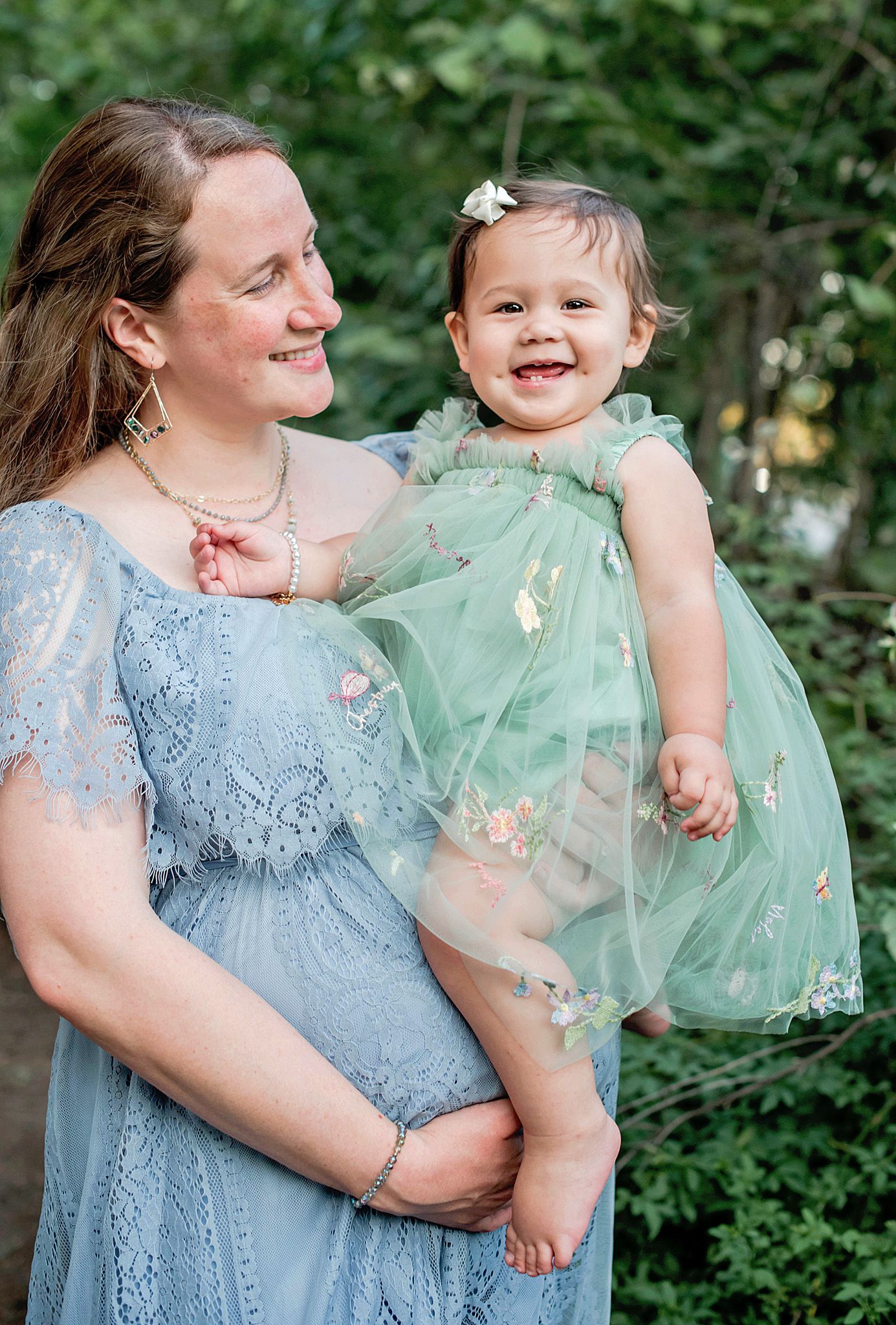 Mother and daughter share joyful moments in matching blue and mint green dresses against a natural backdrop in Driftwood, TX.