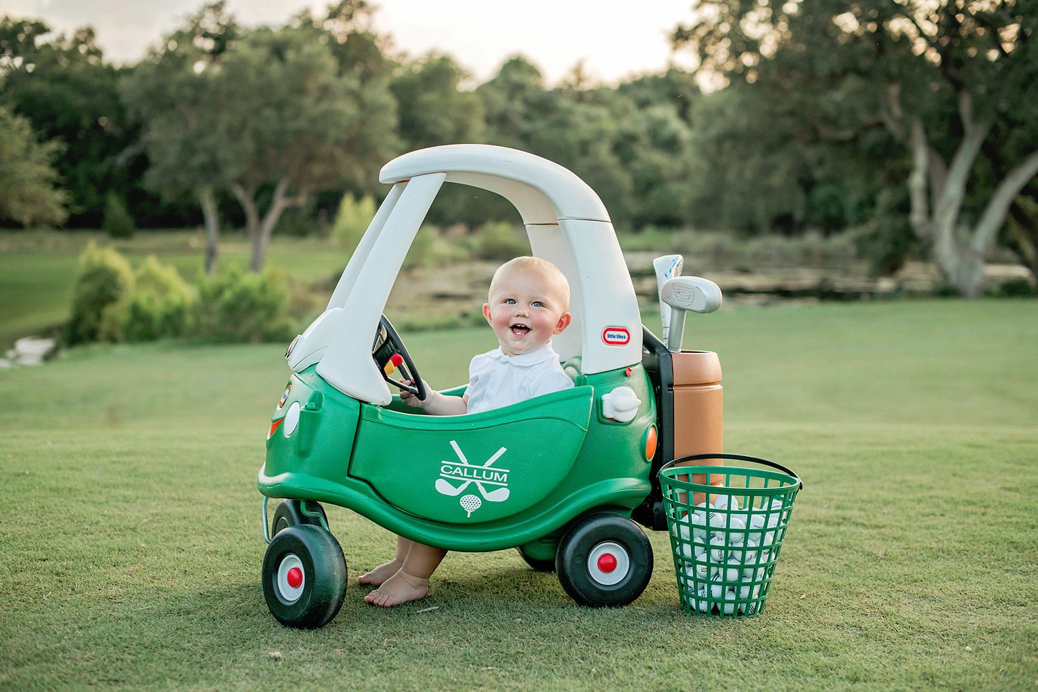 A small toy cozy coupe car in green with a butterfly design sits on grass in a backyard during golden hour.