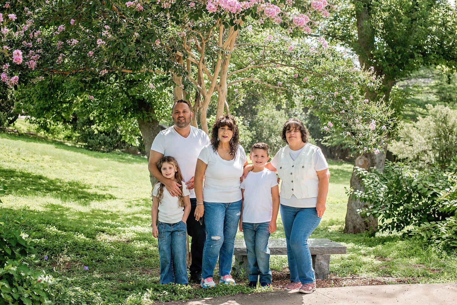 A group of people in coordinated white and denim outfits pose together outdoors in a lush garden setting in Blanco, TX.