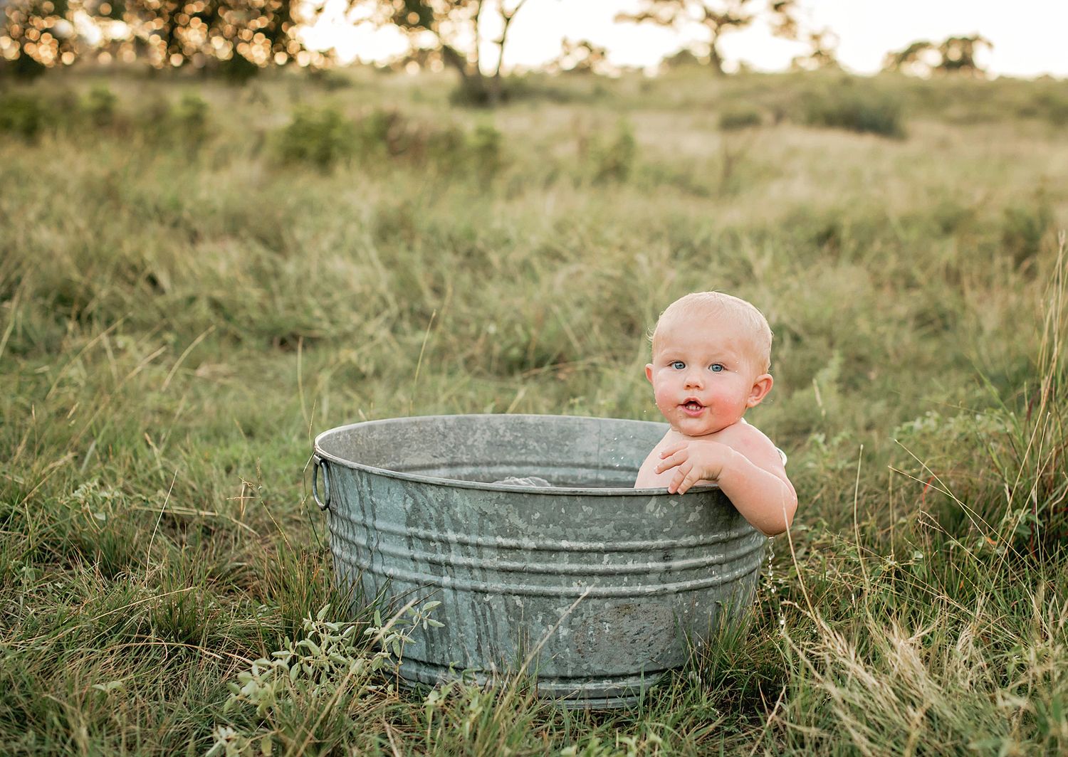 Metal washtub sits in sunlit grassy field at golden hour for rustic photography session.