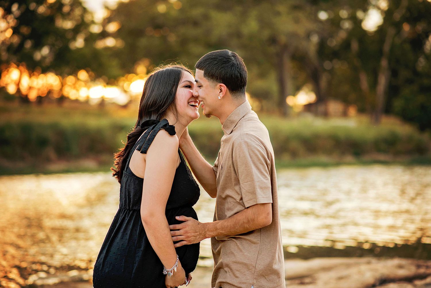 A romantic couple shares tender moments during a sunset photoshoot by a lake in warm golden light.