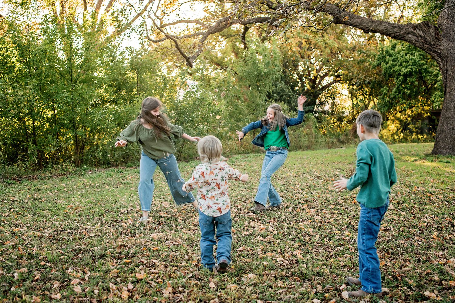 Family members playfully toss autumn leaves in a sunlit park during a golden hour photo session.