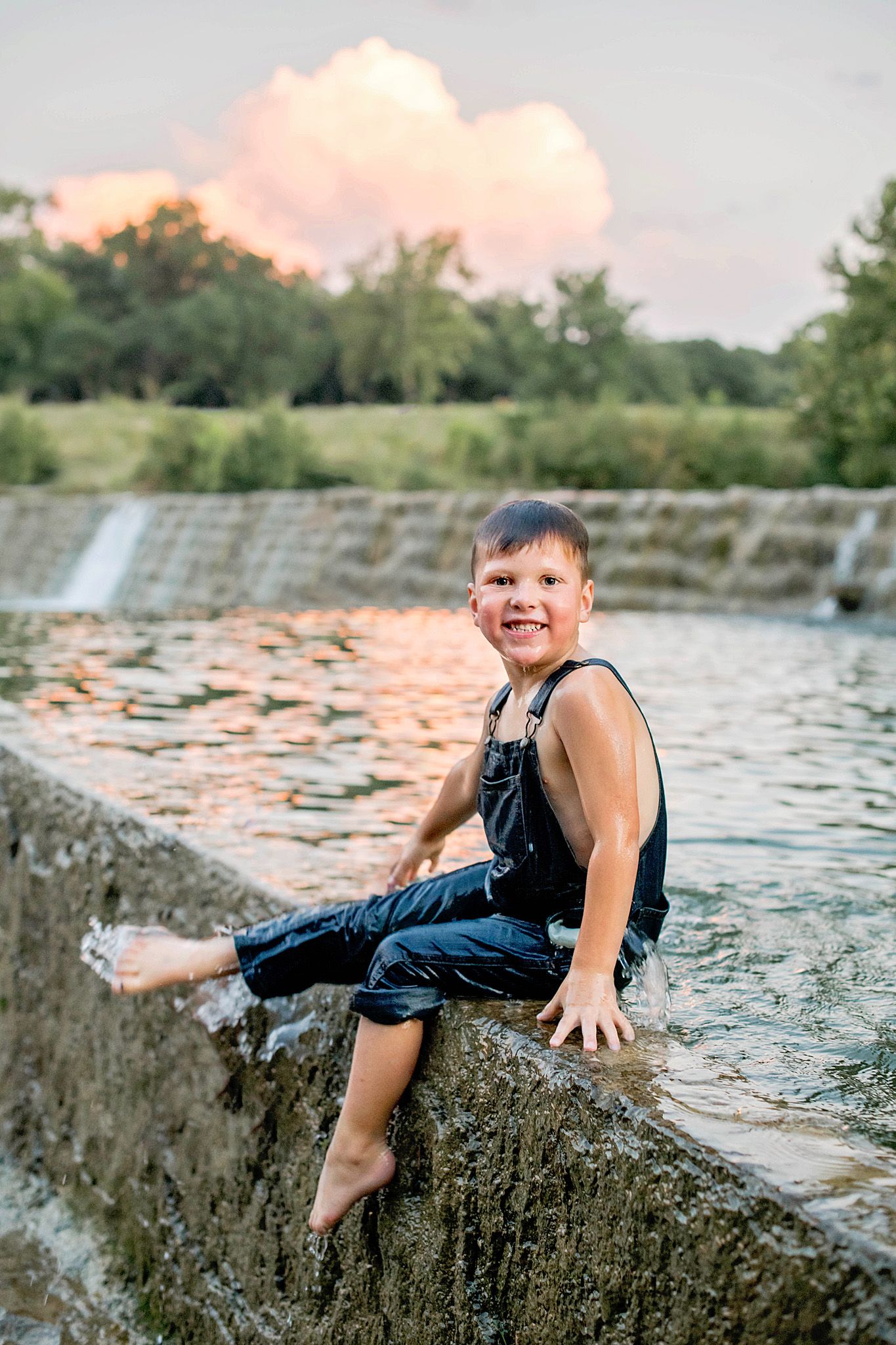 A child plays and poses on rocks near a waterfall during sunset creating a playful outdoor scene.