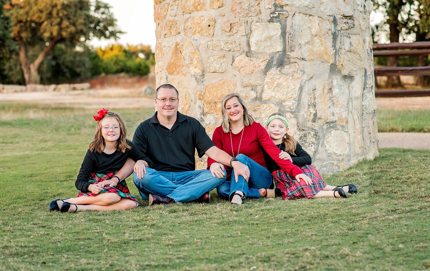 Family members lounging together on grass near stone wall during golden hour outdoor photo session.