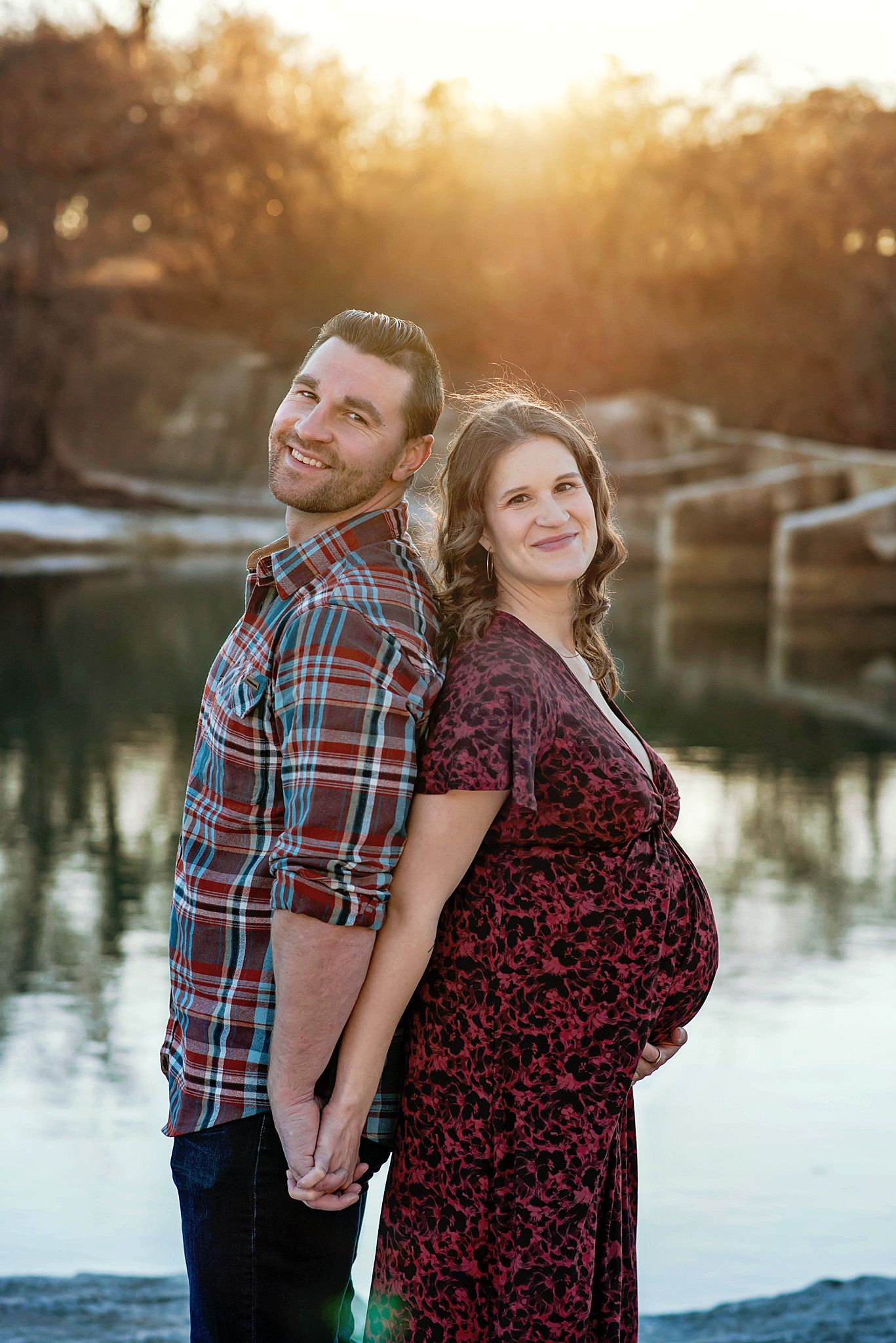 A couple poses together by a lake during golden hour sunset in a romantic outdoor photoshoot.