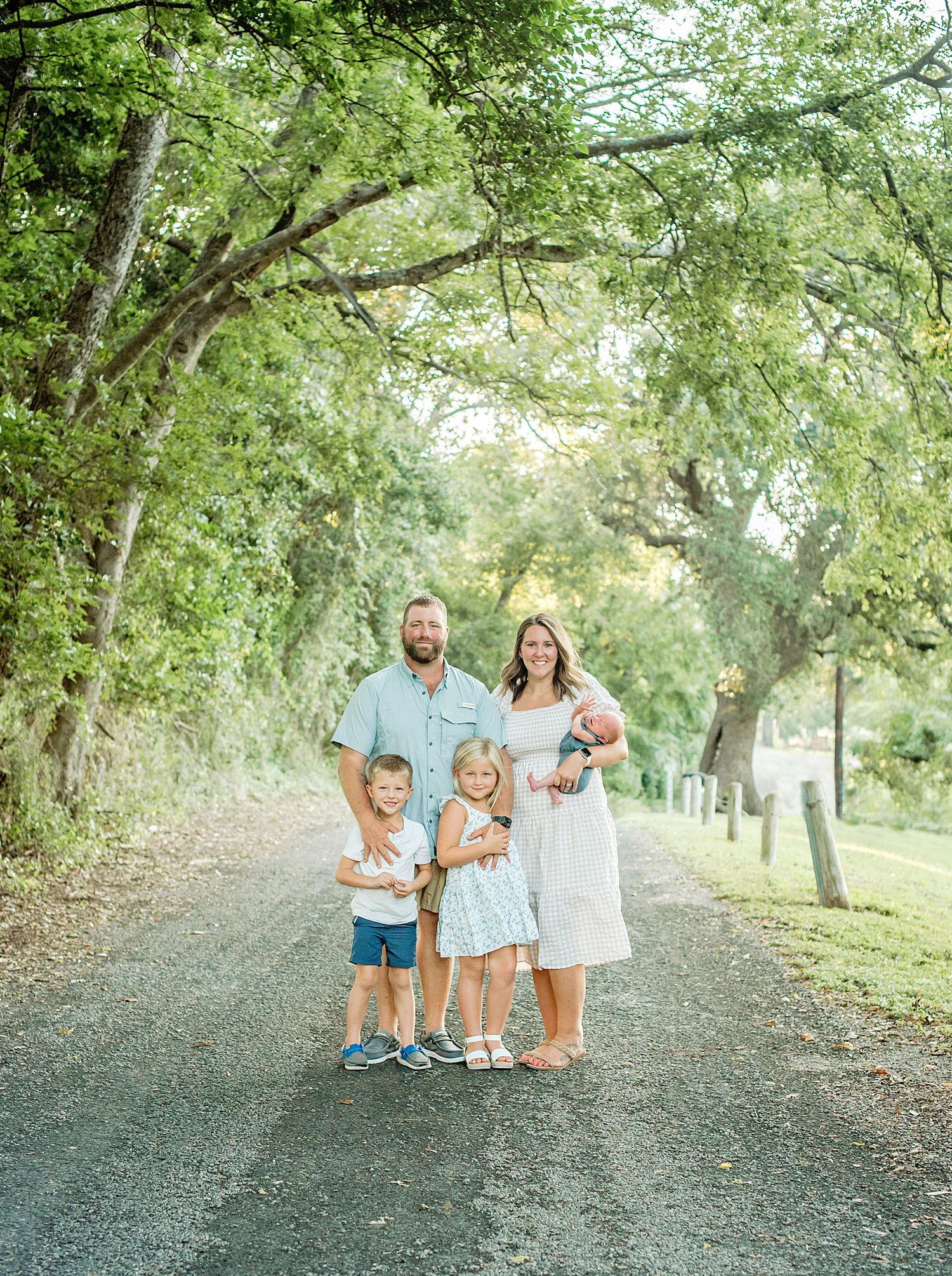 A group stands together on a tree-lined gravel path on a bright summer day.