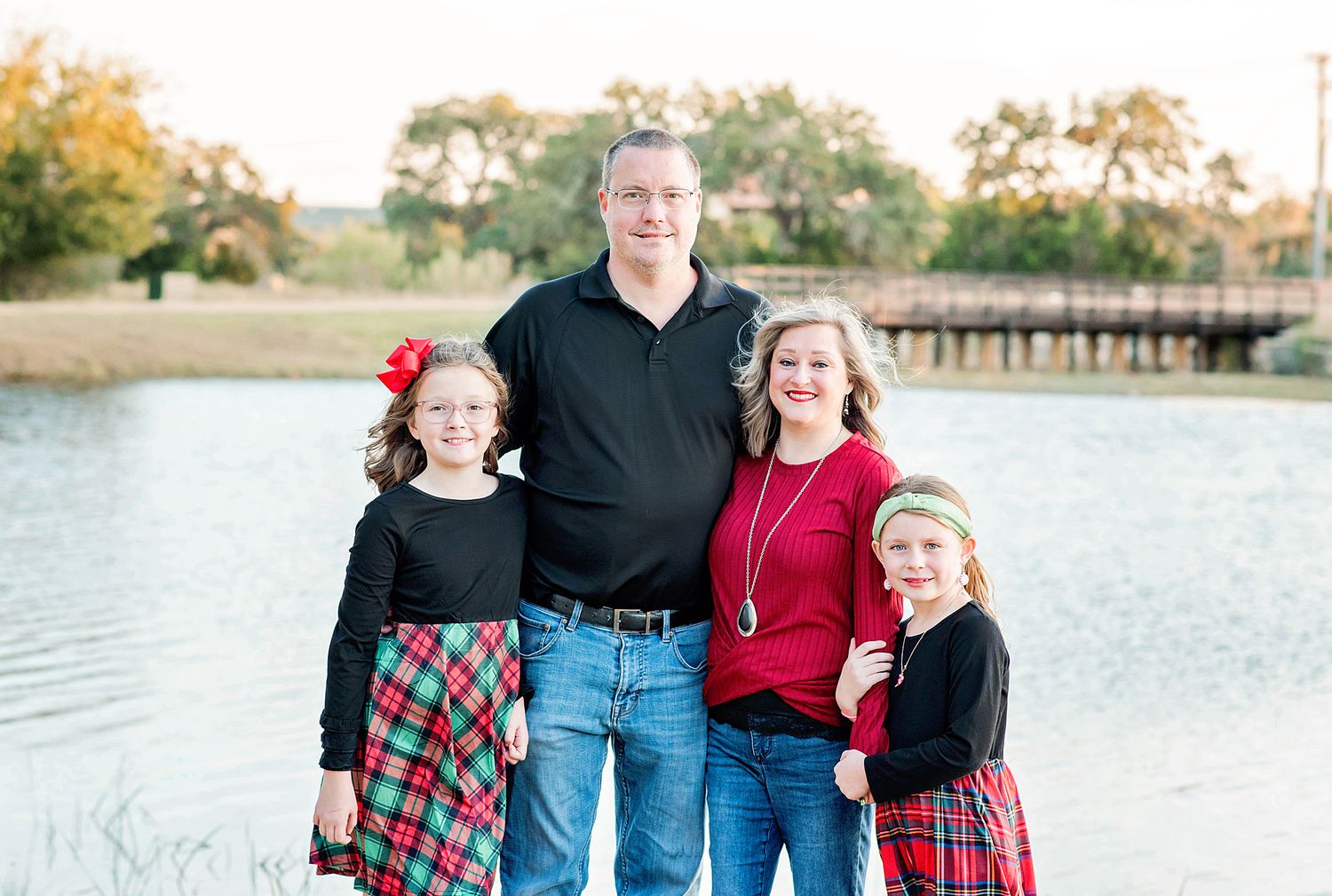 Family wearing coordinated red and blue outfits poses together by a scenic lake at sunset.