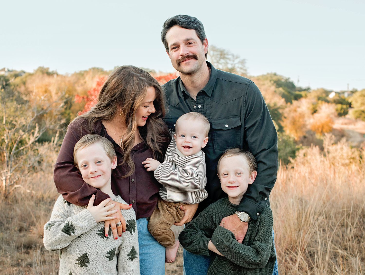 A family group poses together outdoors during golden hour in a natural setting.