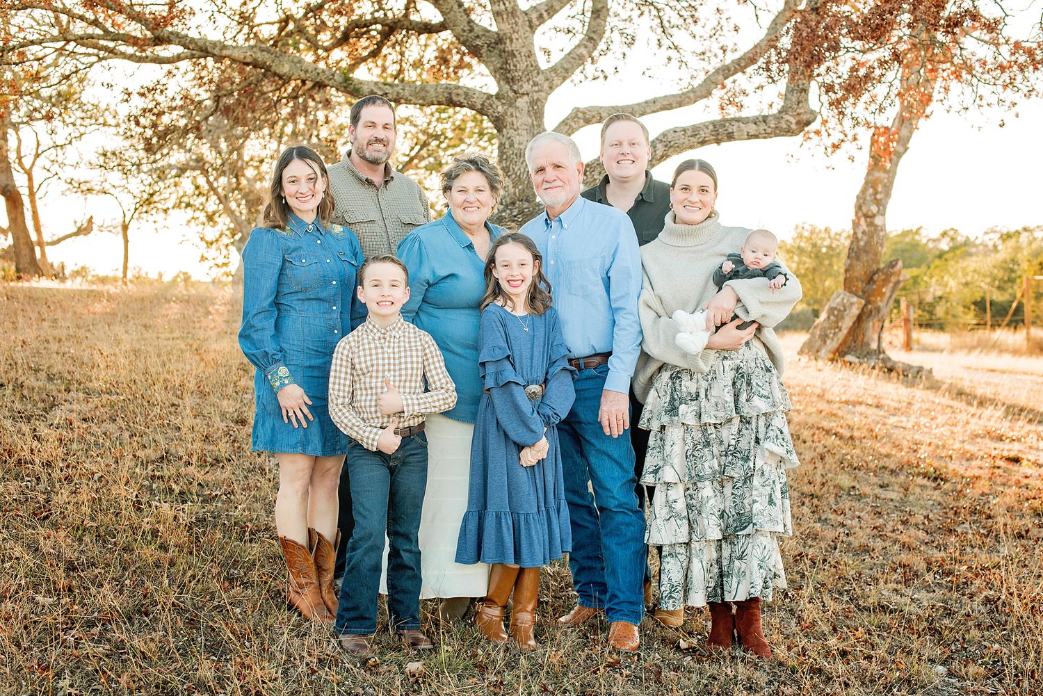 A group wearing coordinated blue and gray outfits poses together in a sunlit outdoor setting with autumn leaves.