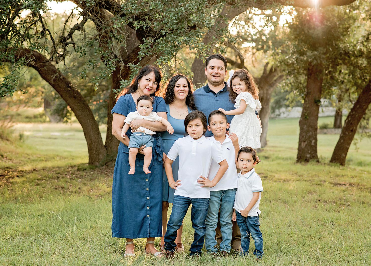 A series of outdoor family portraits taken in a grassy park with oak trees at sunset in Blanco, TX.
