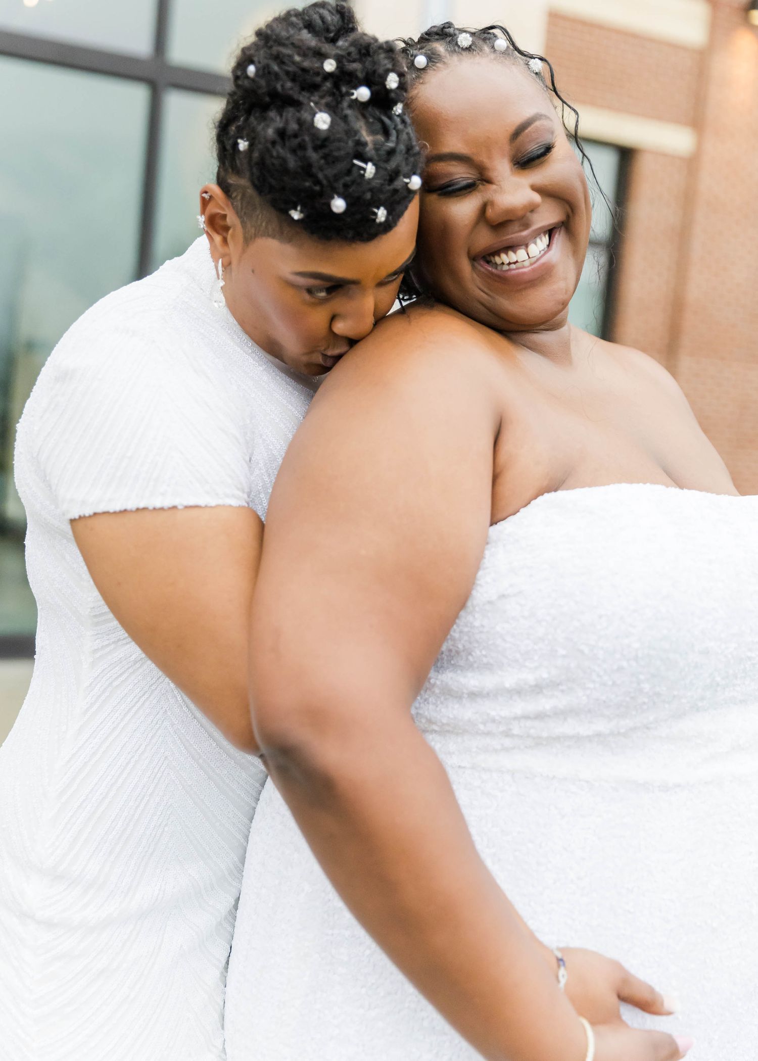 Two people in white dresses sharing a joyful embrace during their wedding celebration.