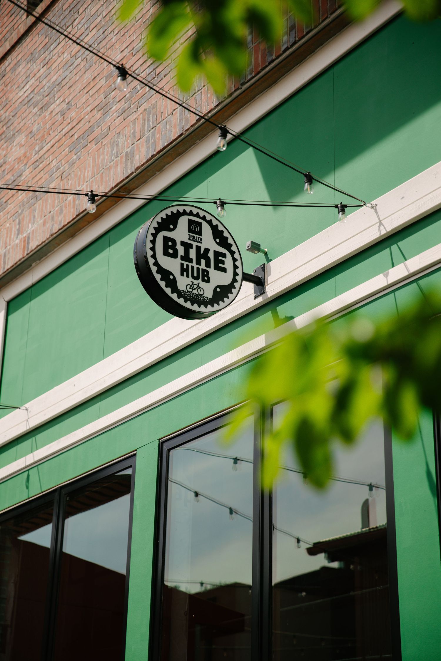A bike shop sign mounted on a green wall with blurred foliage in the foreground.