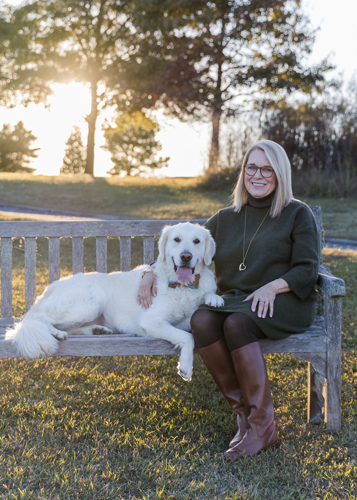 White dog and person relaxing on wooden bench during golden hour sunset.