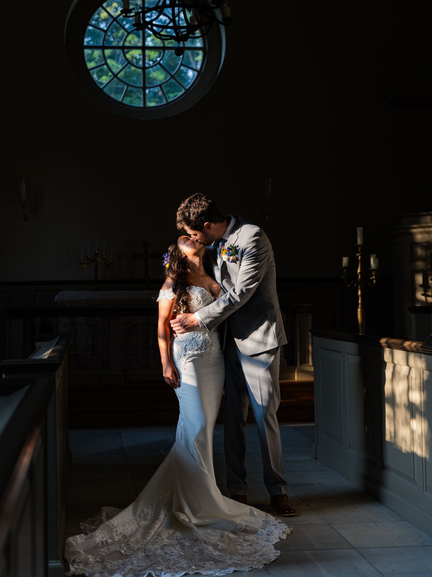 A romantic wedding moment captured in a church with a stained glass window and dramatic lighting.