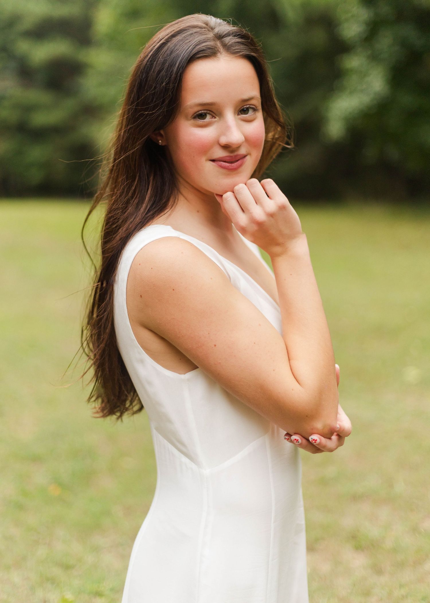 Person in white sleeveless dress poses playfully in a sunny outdoor field.