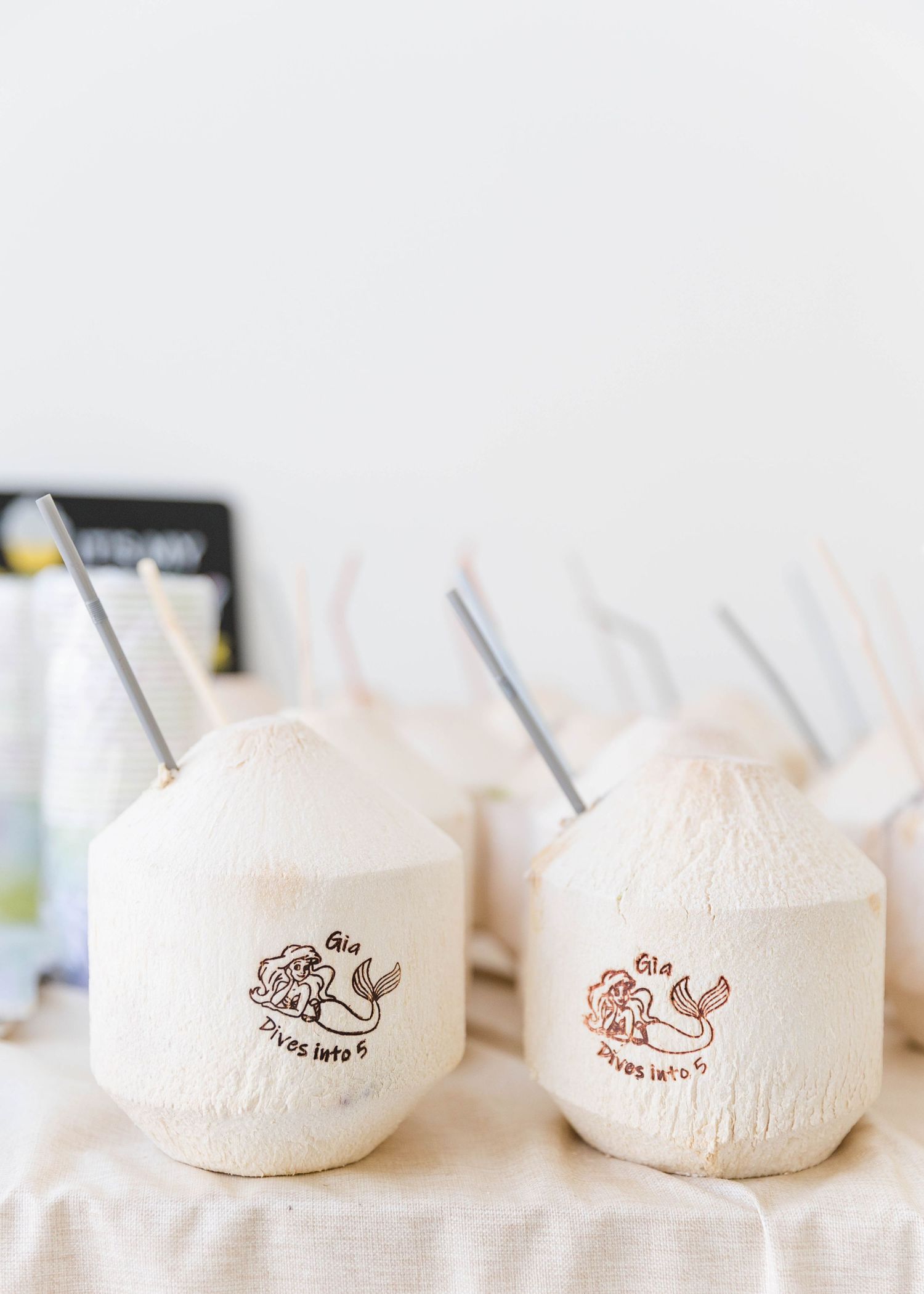 Row of fresh coconuts with branded logos arranged on white surface.