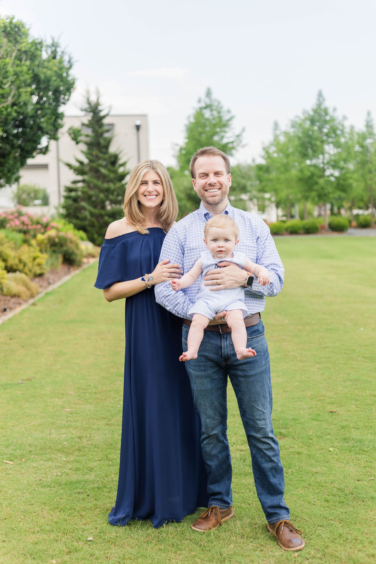 Family portrait in a green park setting with baby wearing light blue outfit.