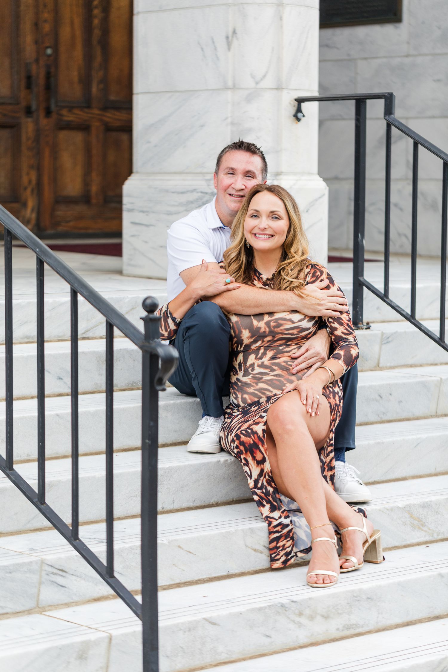 A couple sitting on white marble steps wearing casual clothing and animal print dress.