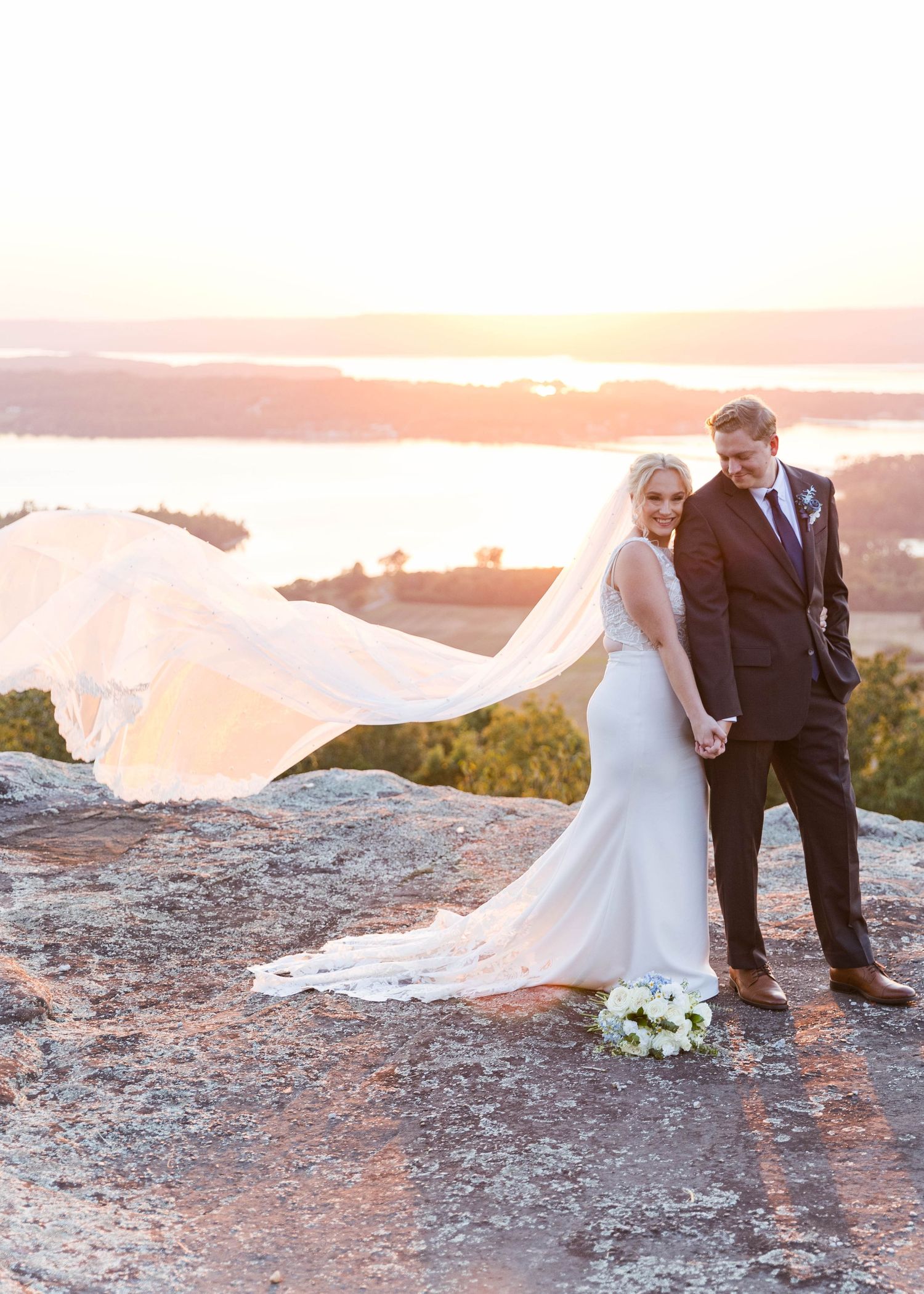 Romantic sunset wedding portrait on rocky terrain with flowing veil.