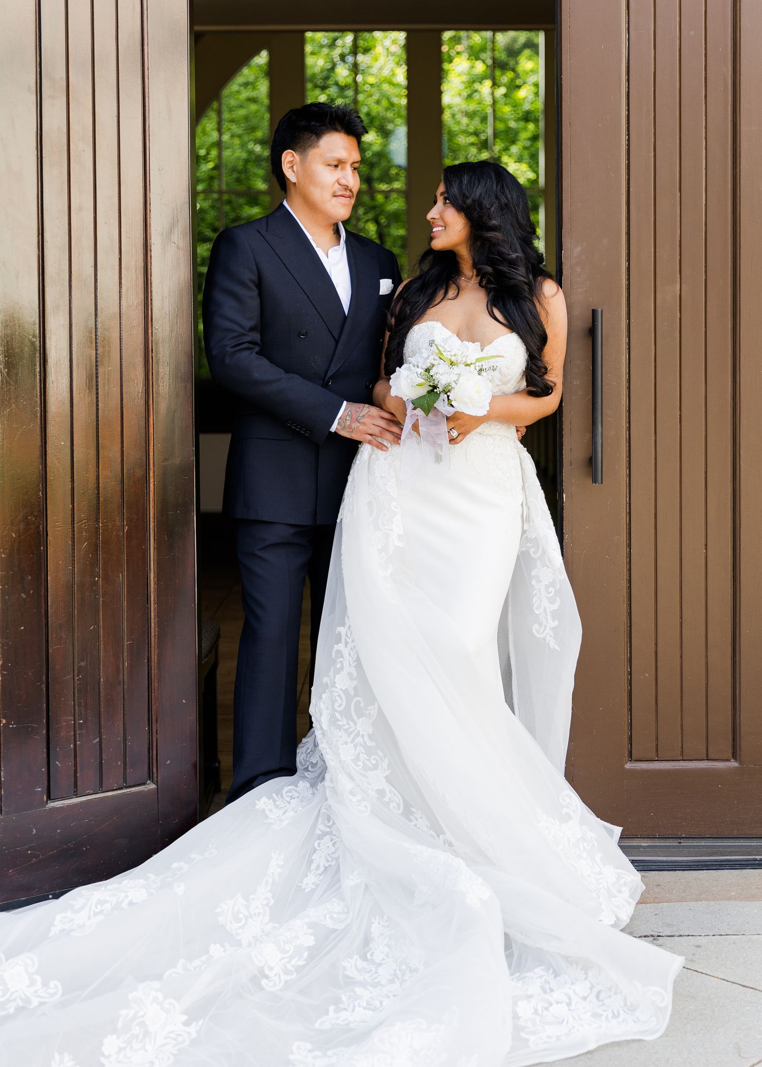 Elegant couple in wedding attire pose together in front of the wooden doors of the beautiful Ashton Gardens in Atlanta, Georgia.