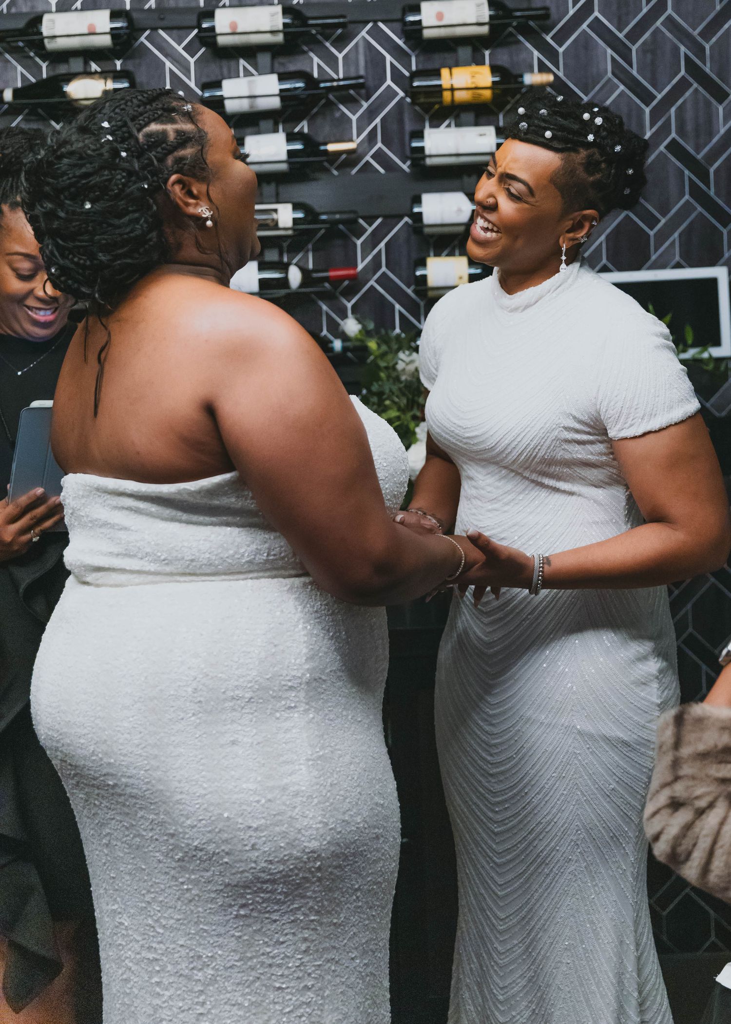 Two people in grey outfits sharing a joyful moment against a patterned wall background.