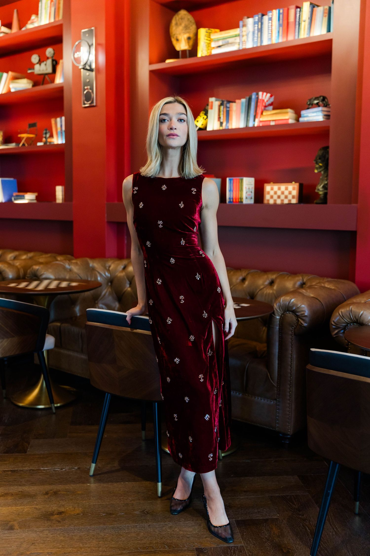Burgundy velvet dress with floral details styled in library setting with red bookshelves.
