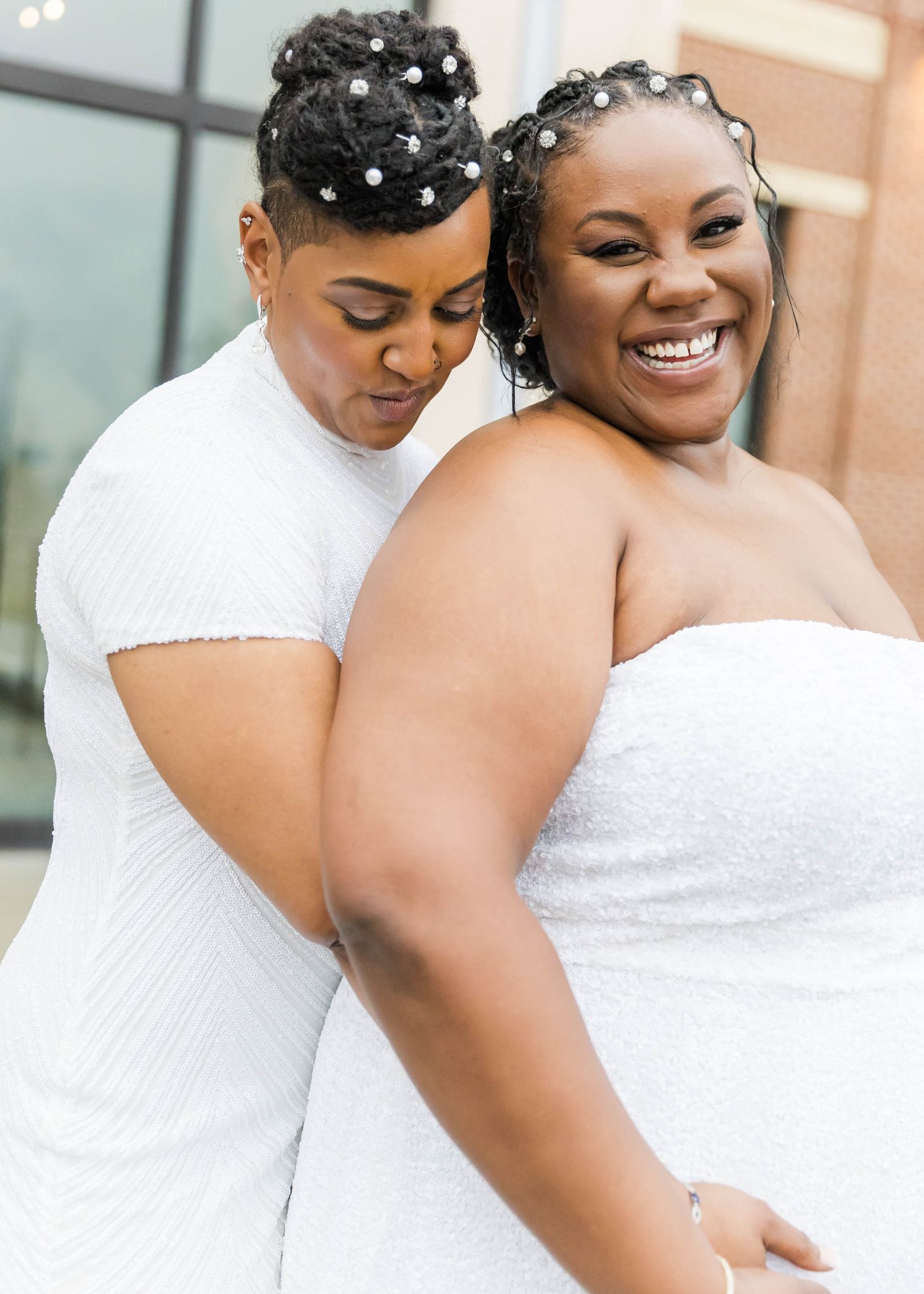 Two people in matching white dresses share a joyful moment together.