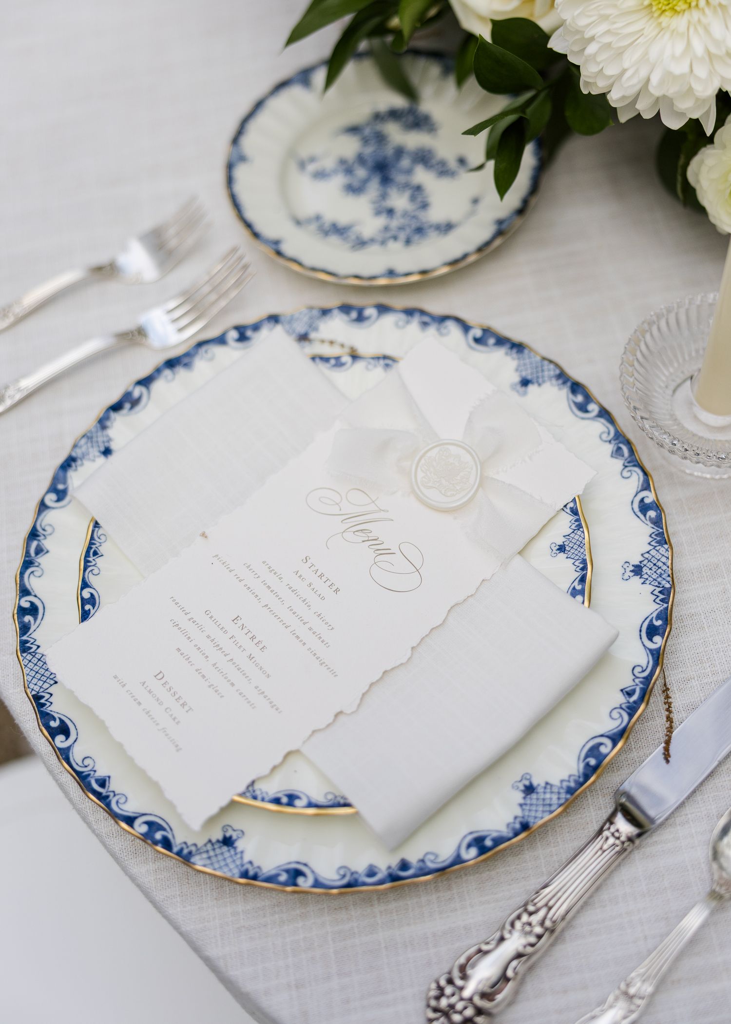 Elegant blue and white china plate with a wedding menu card sealed with a wax seal on a formal table setting.