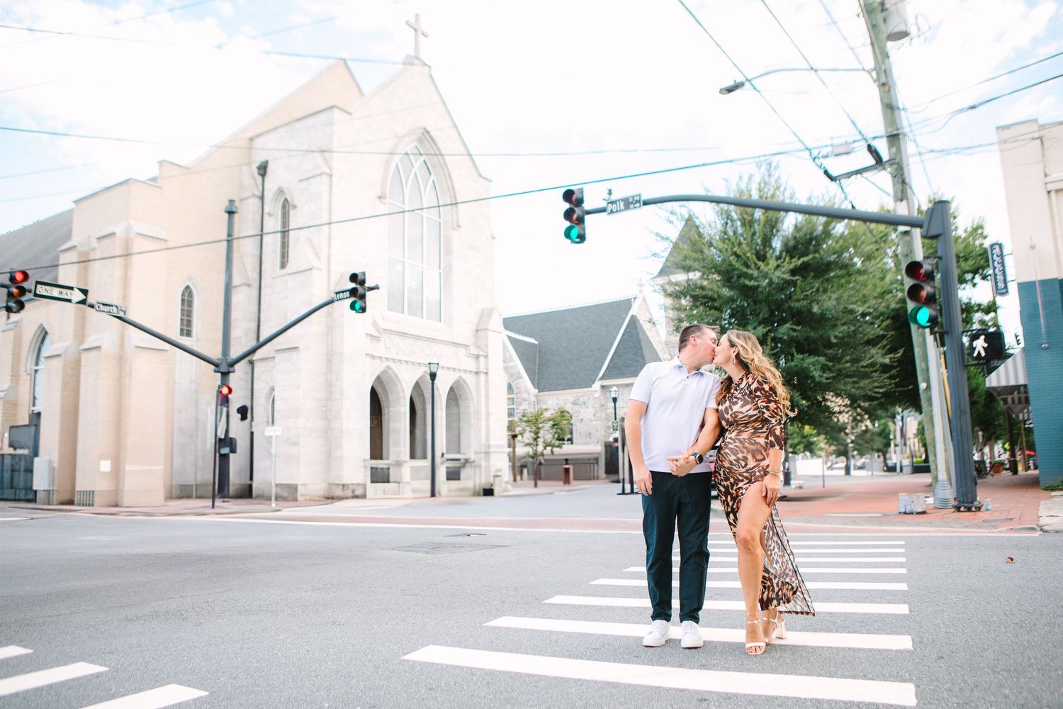 Couple kissing at a crosswalk in front of a white church in a charming downtown street setting.