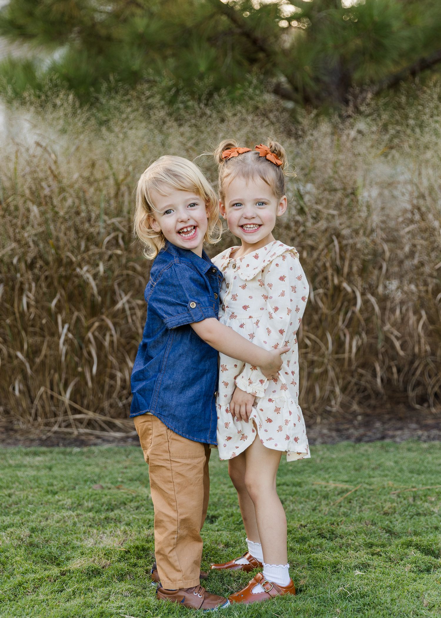 Two young children hugging and playing together on green grass.