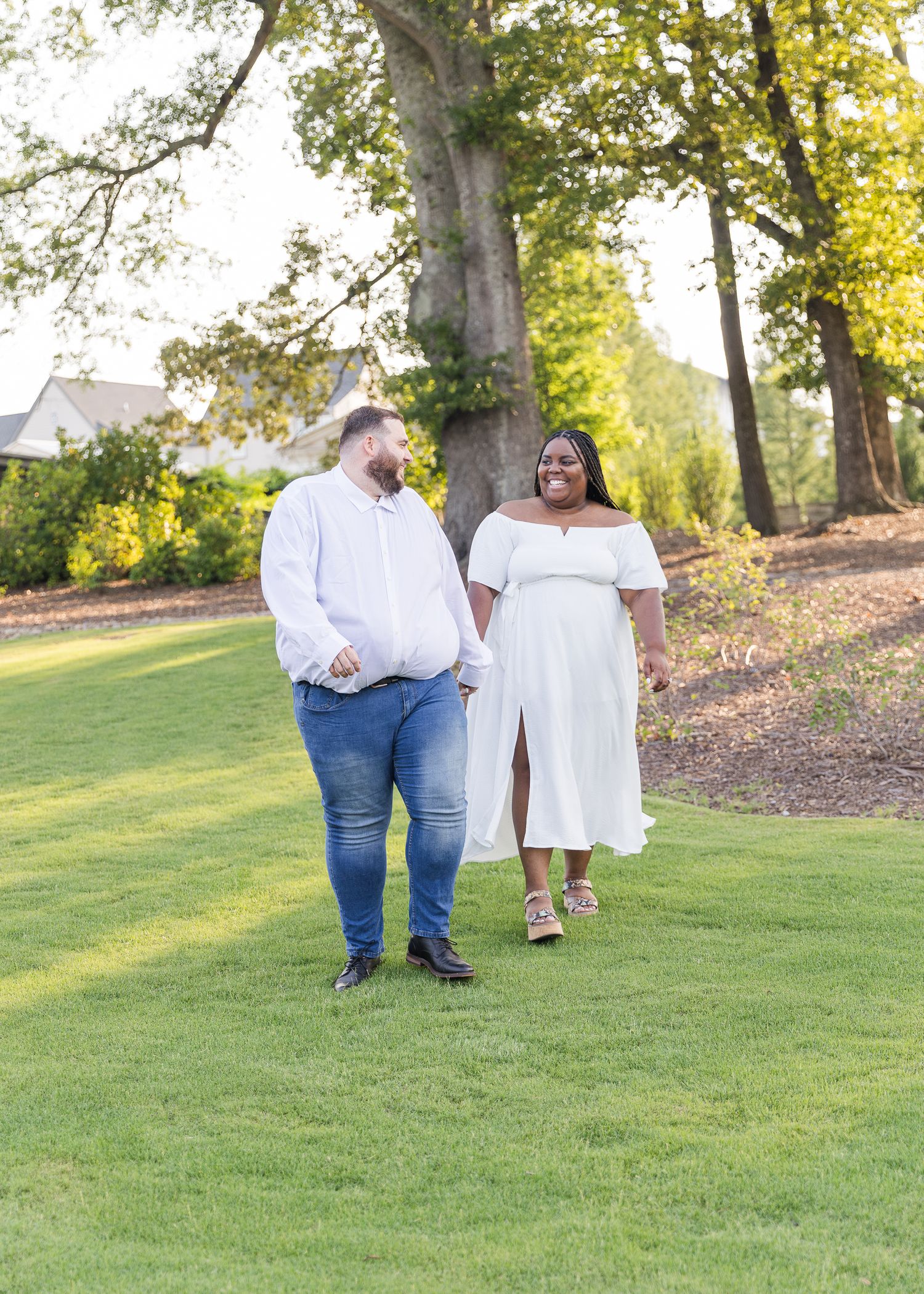 A couple in white outfits walking together on a sunlit grassy hill.