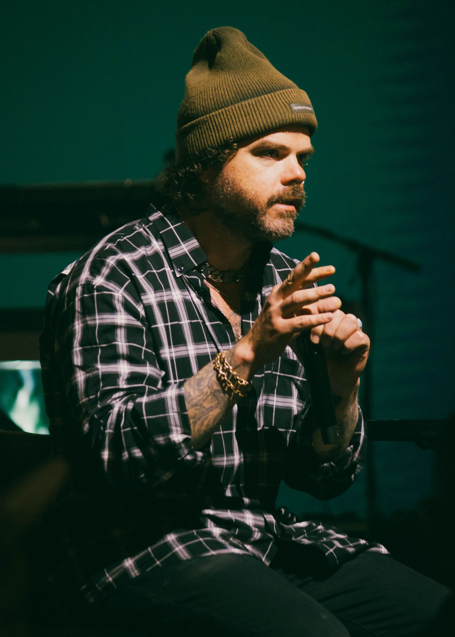 Person in plaid shirt and beanie performing in dramatic lighting.