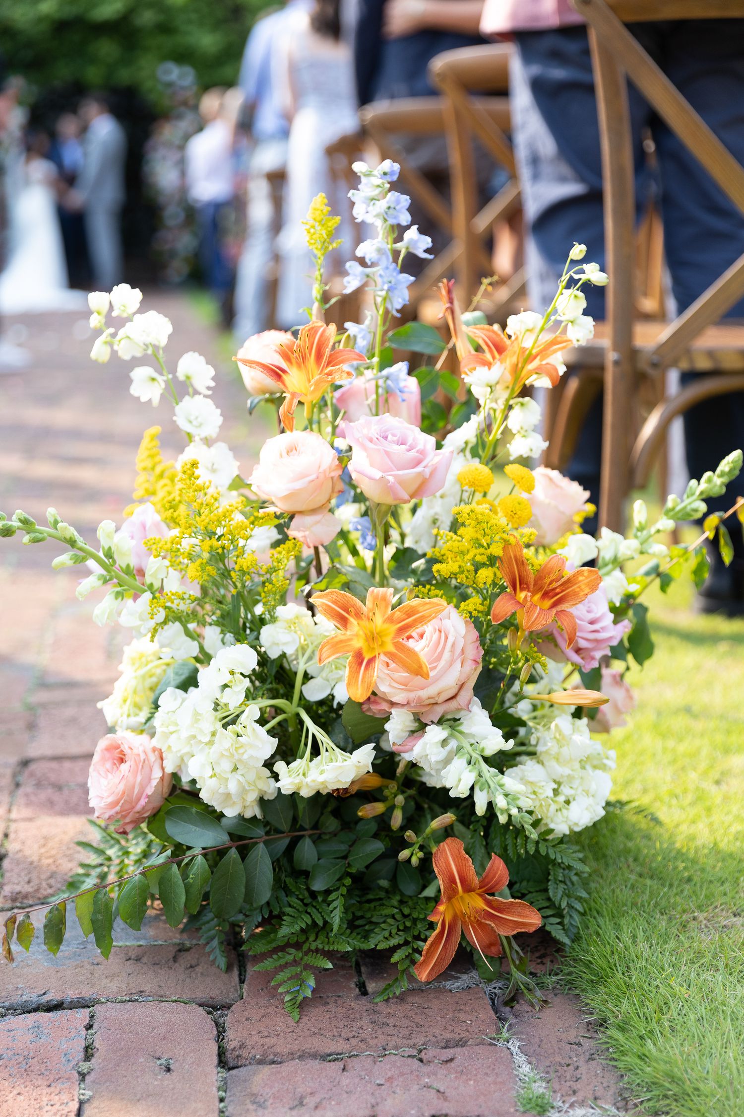 Romantic floral arrangements with peach, yellow and white blooms line outdoor wedding aisle.