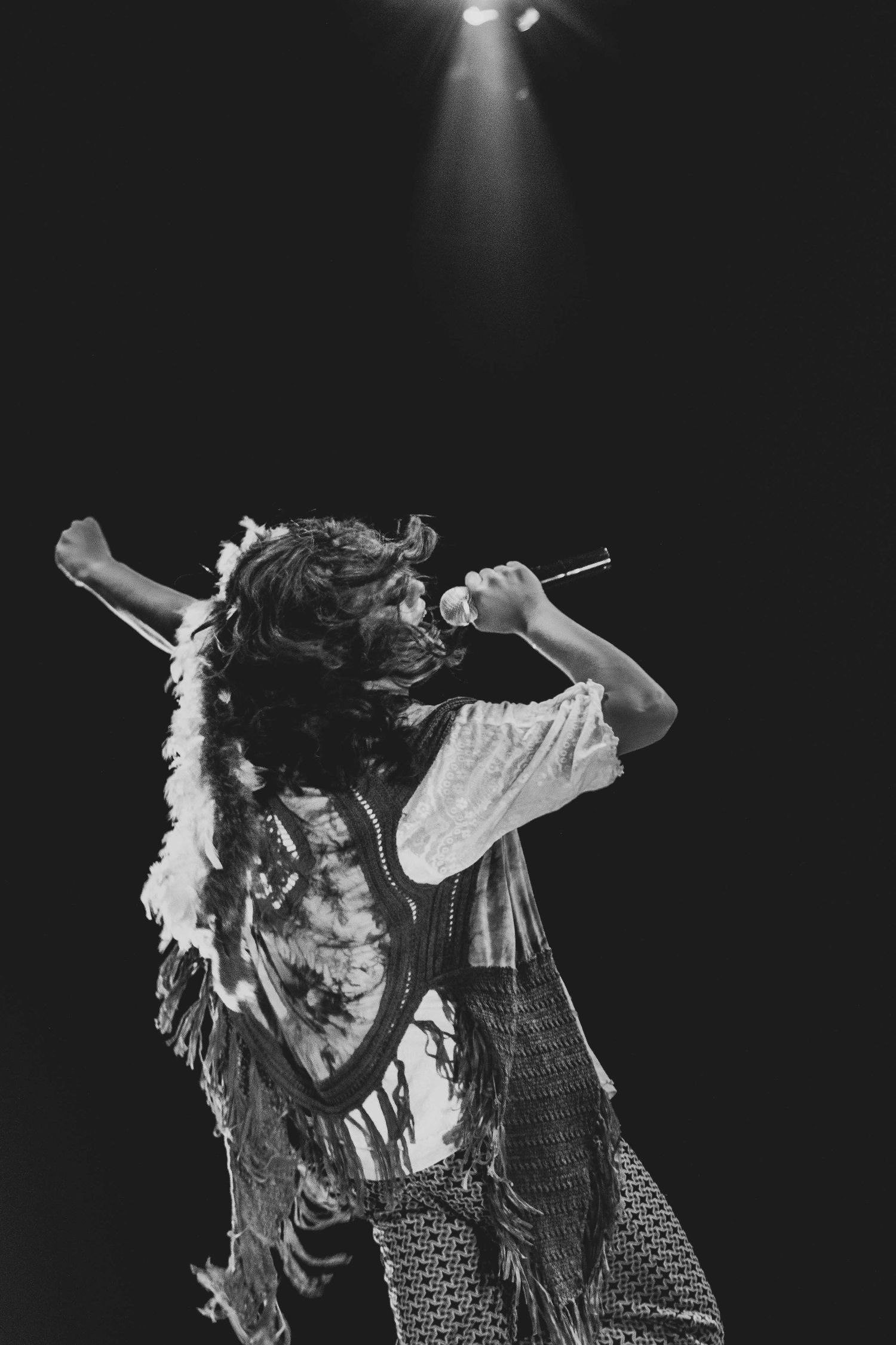 Performer in feathered costume dancing under spotlight on dark stage.