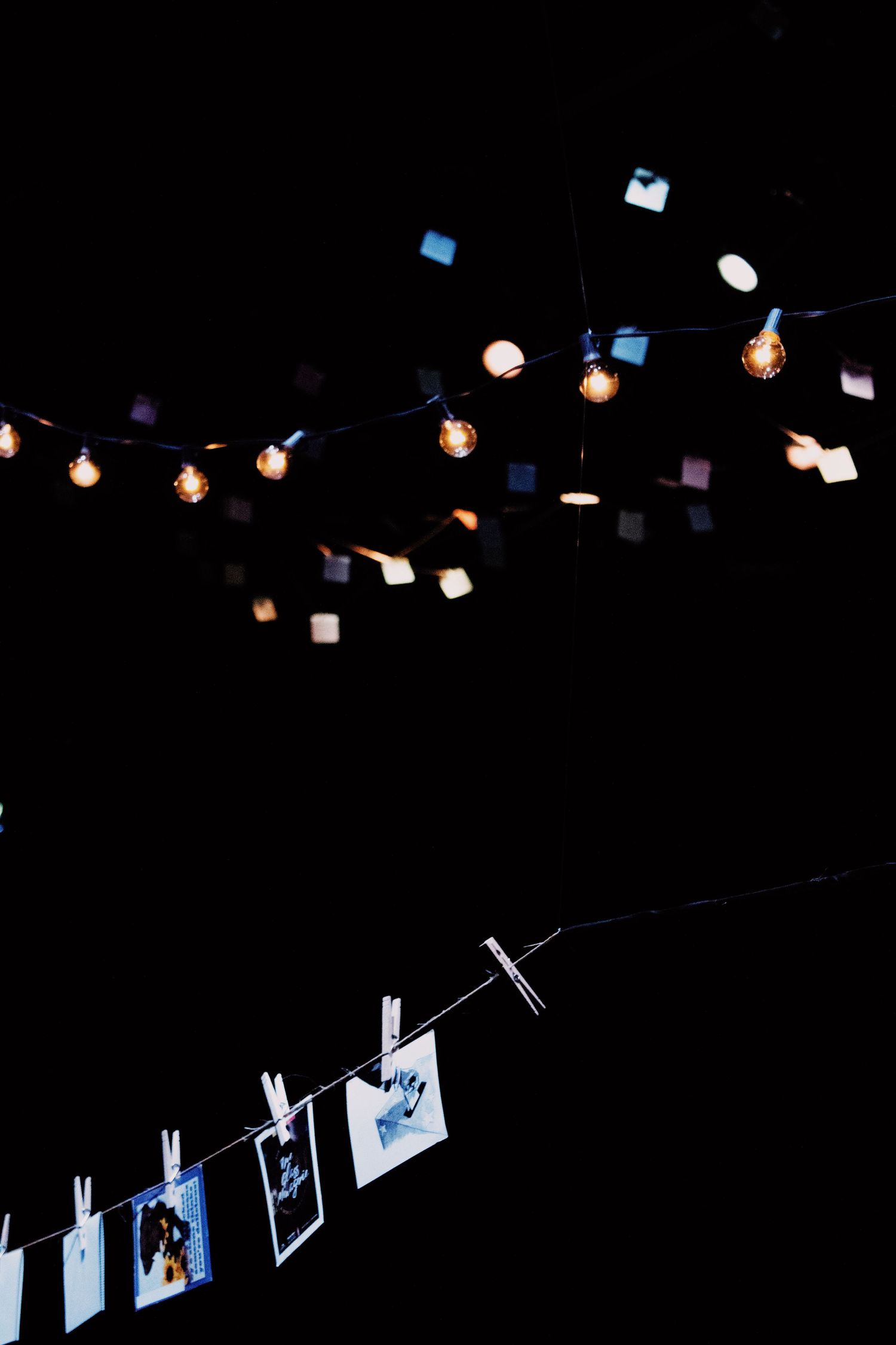 String lights illuminate a display of photos hung with clothespins against a dark background.