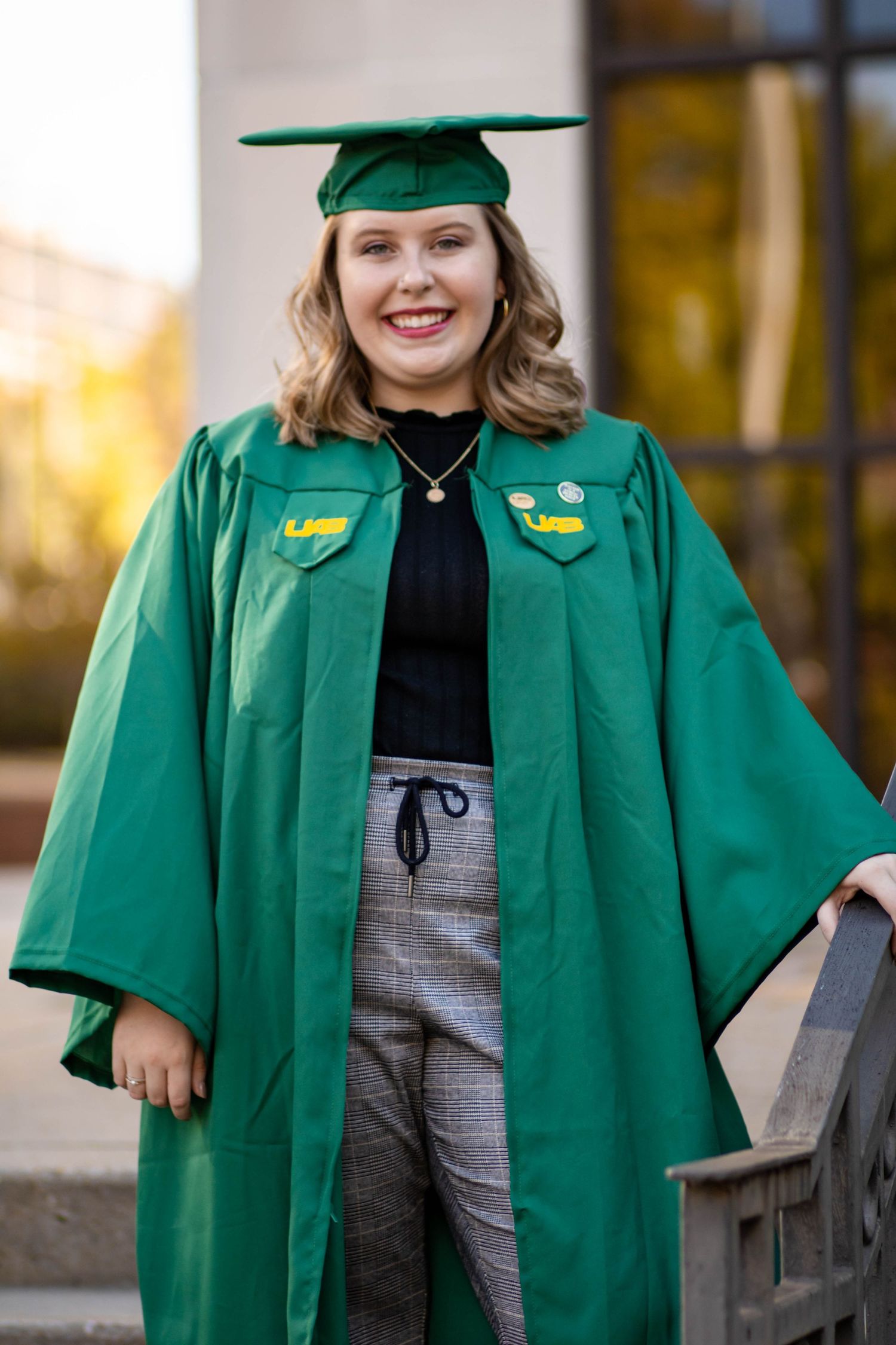 Graduate wearing emerald green academic regalia poses outdoors during commencement.