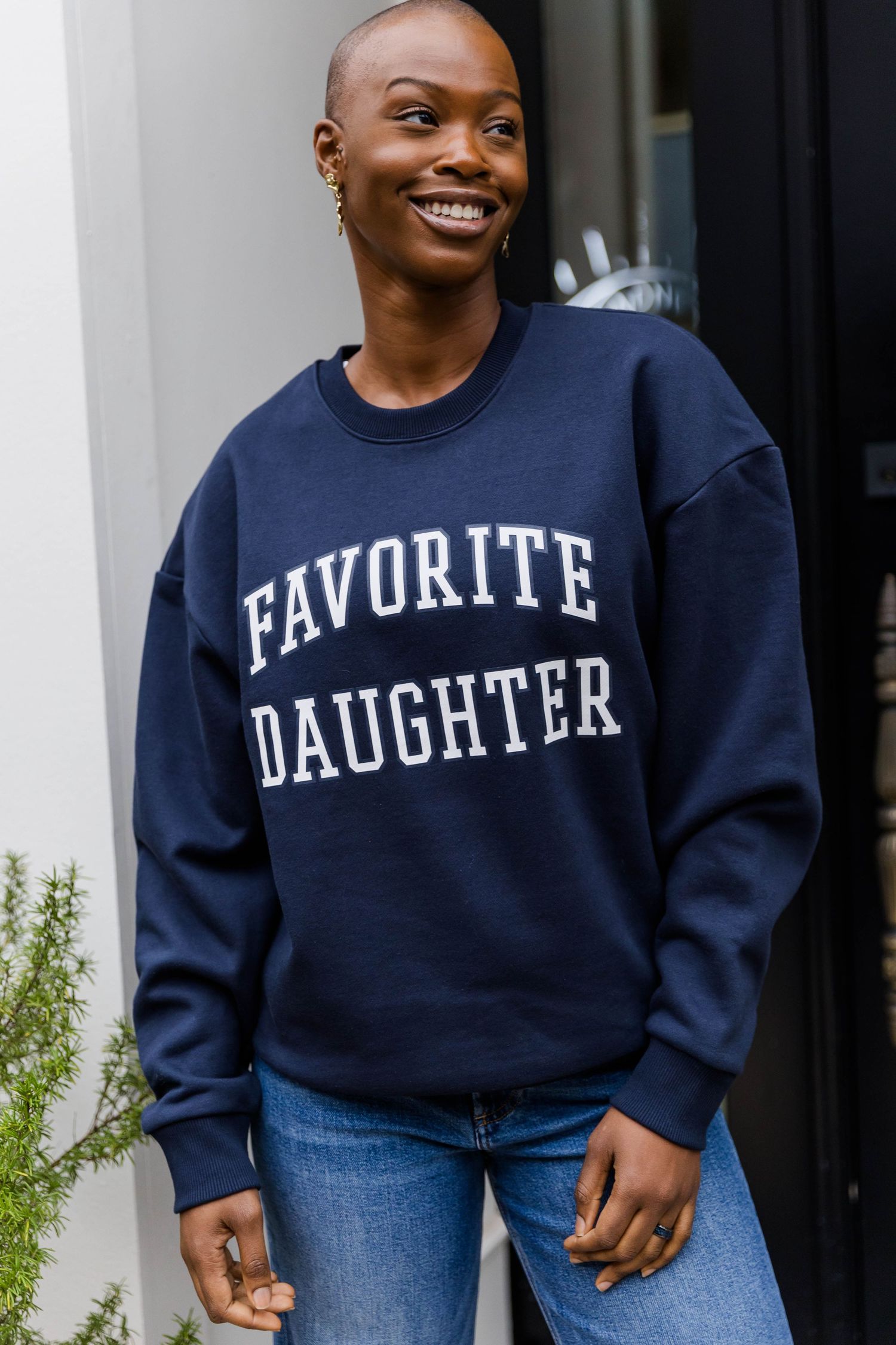 Navy blue sweatshirt with 'Favorite Daughter' text worn with blue jeans in casual street style.