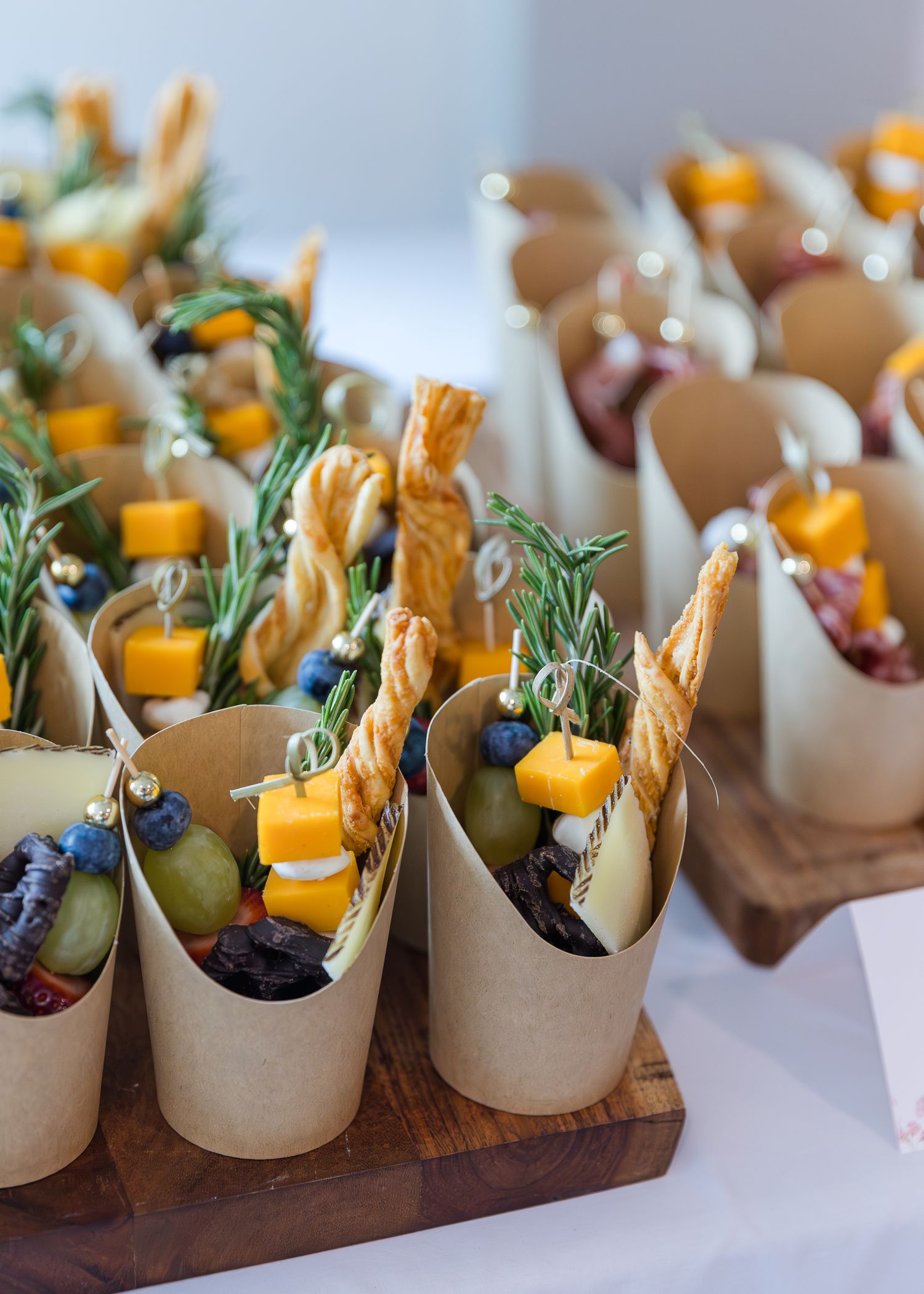 Elegant appetizer cups filled with cheese, herbs and vegetables arranged on wooden serving boards.