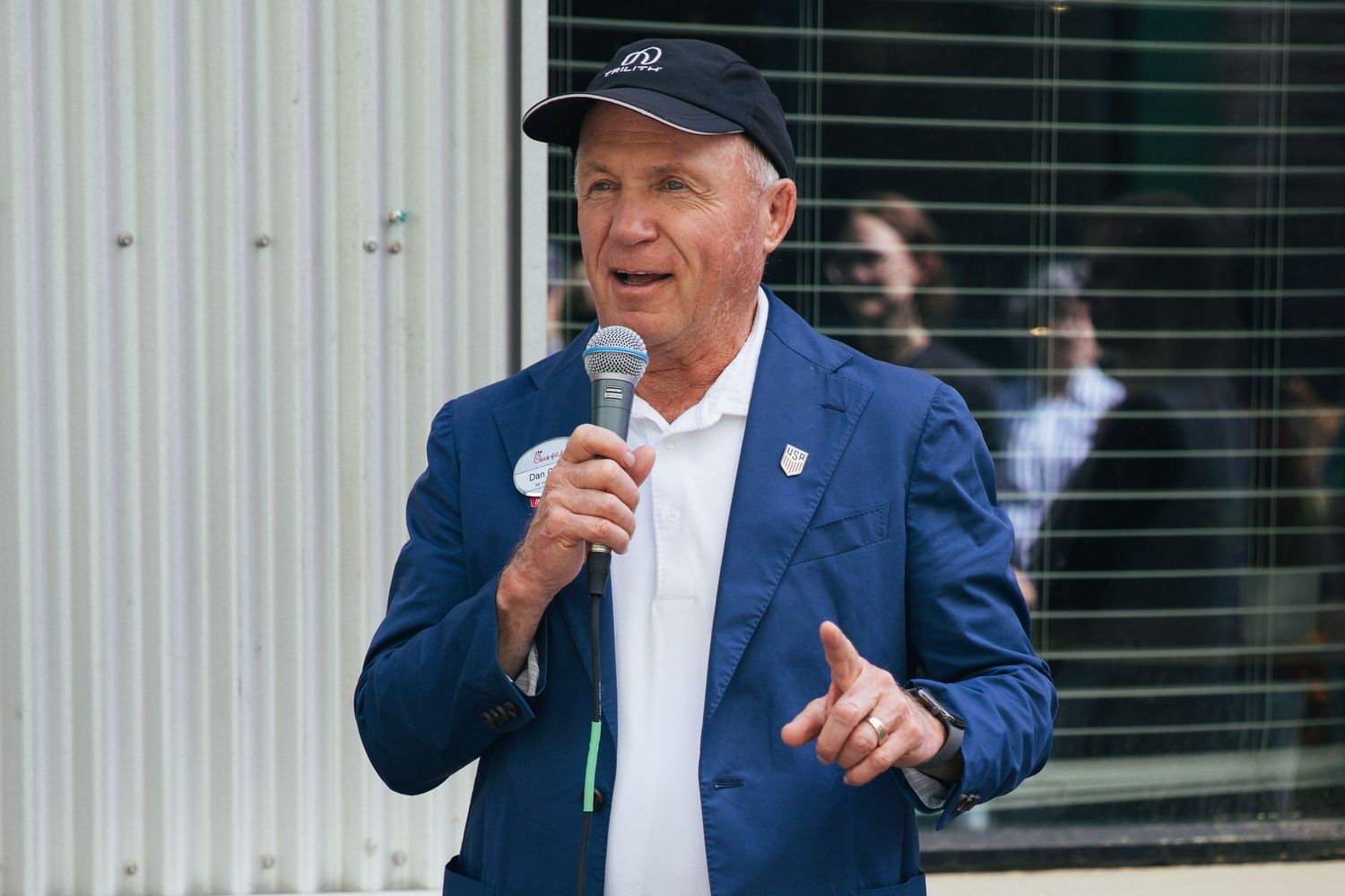 A person in a baseball cap speaking or presenting outdoors.