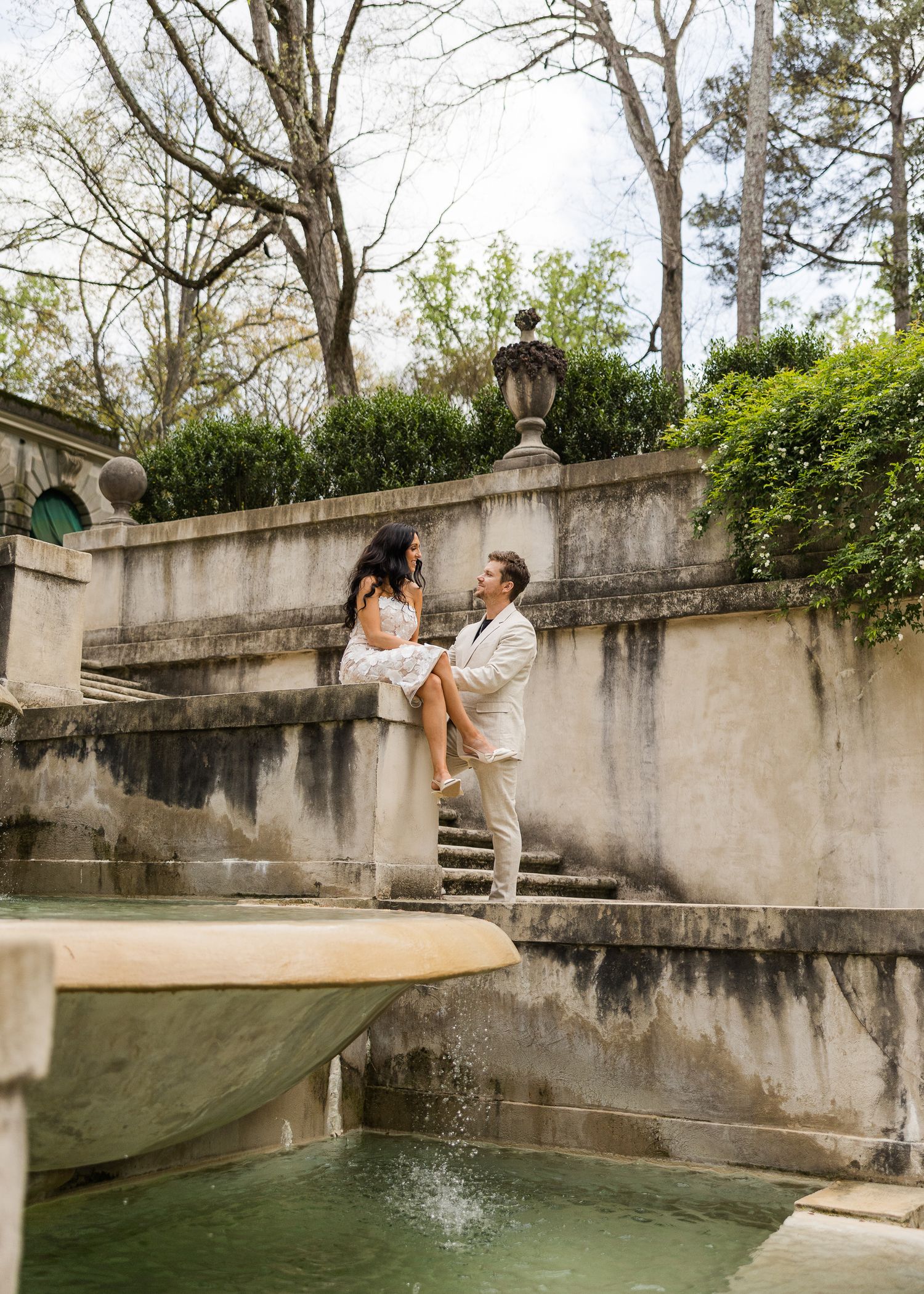 Couple sharing a romantic moment by an elegant stone fountain in a lush garden setting at the Swan House in Atlanta, Georgia