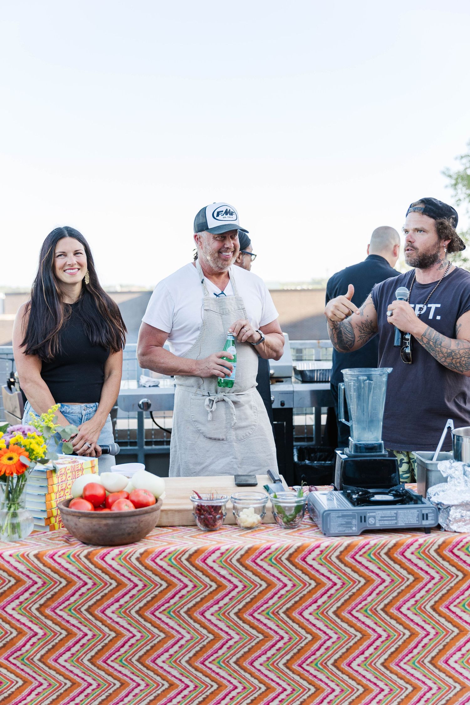 Catering table with colorful chevron pattern tablecloth displaying food and drinks at an outdoor event.