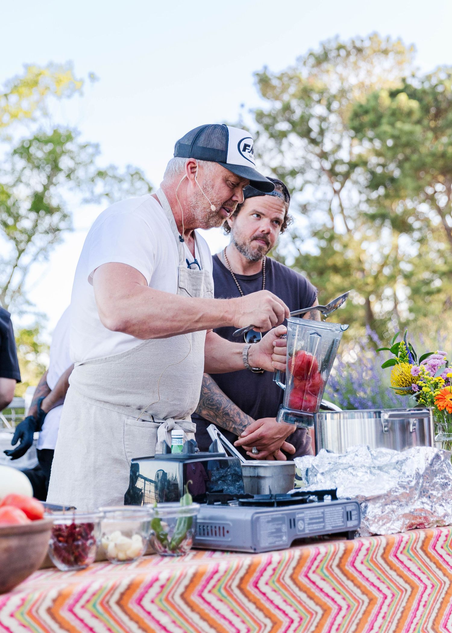 Catering staff preparing food and drinks at an outdoor event with colorful tablecloth.
