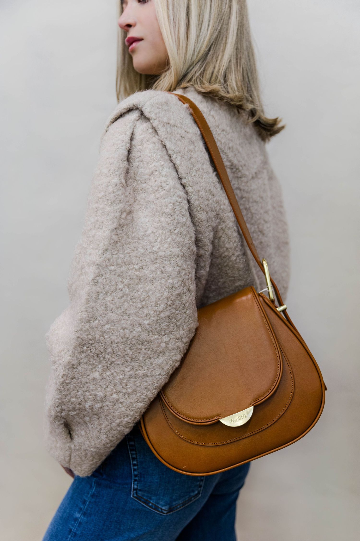 Cozy beige teddy coat styled with brown leather shoulder bag against neutral background.