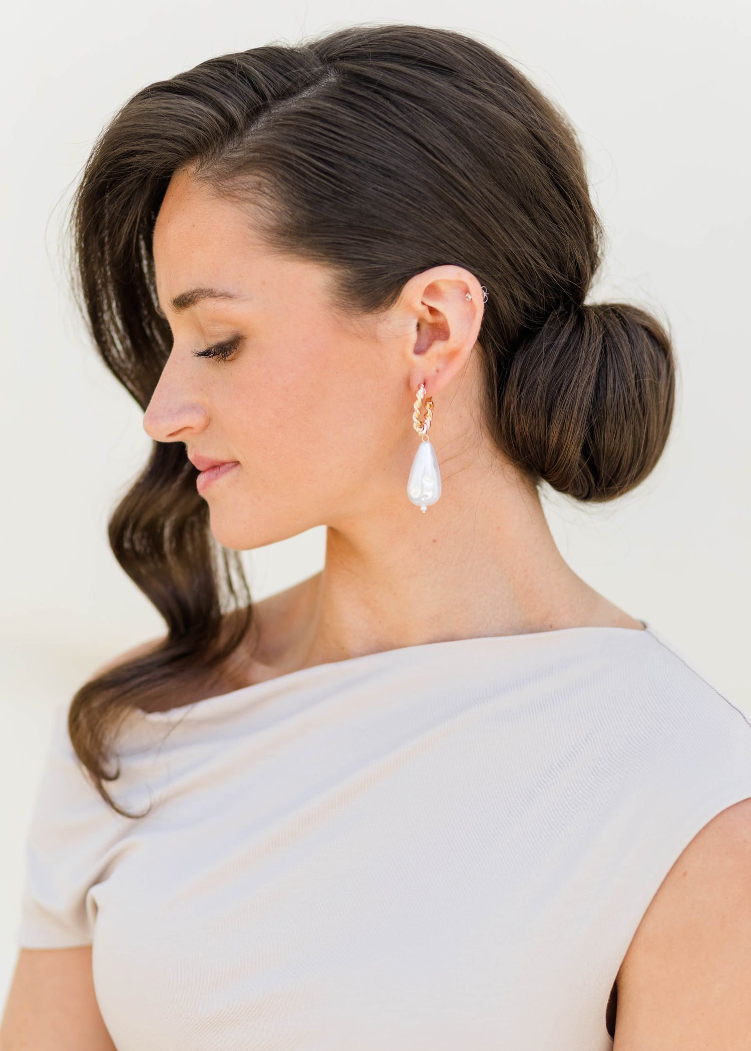 Bride with elegant low bun hairstyle wearing gold and pearl drop earrings in a sleeveless ivory gown.