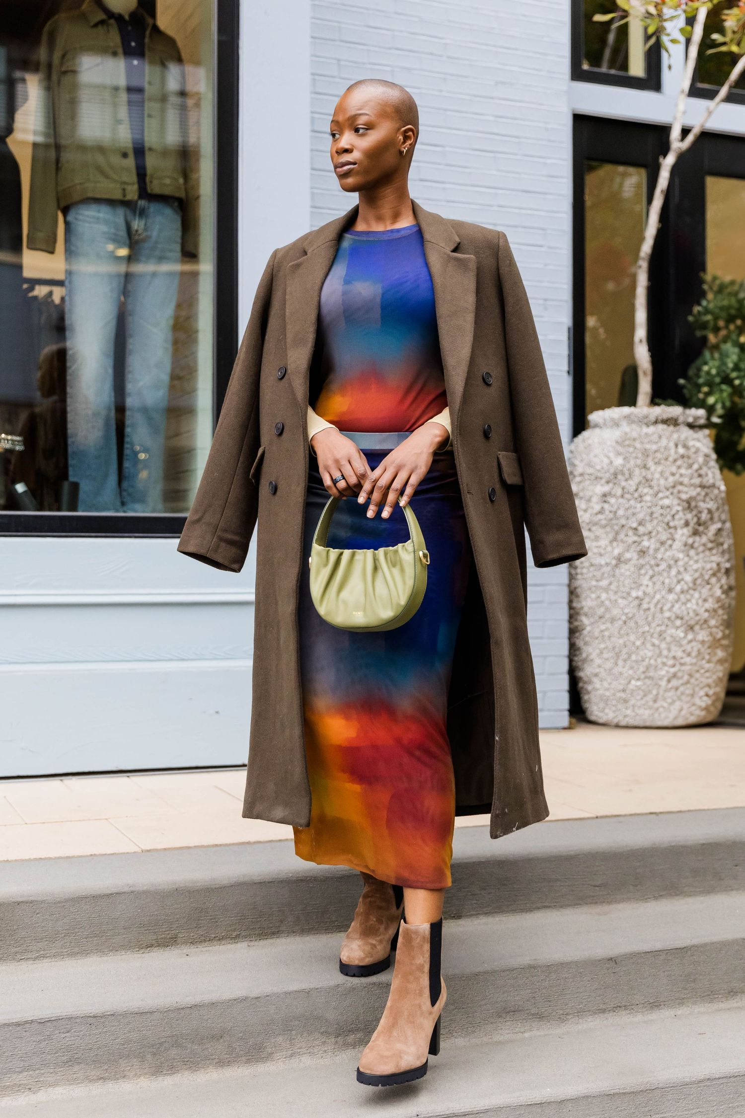Stylish outfit featuring brown coat over gradient dress with small green purse.
