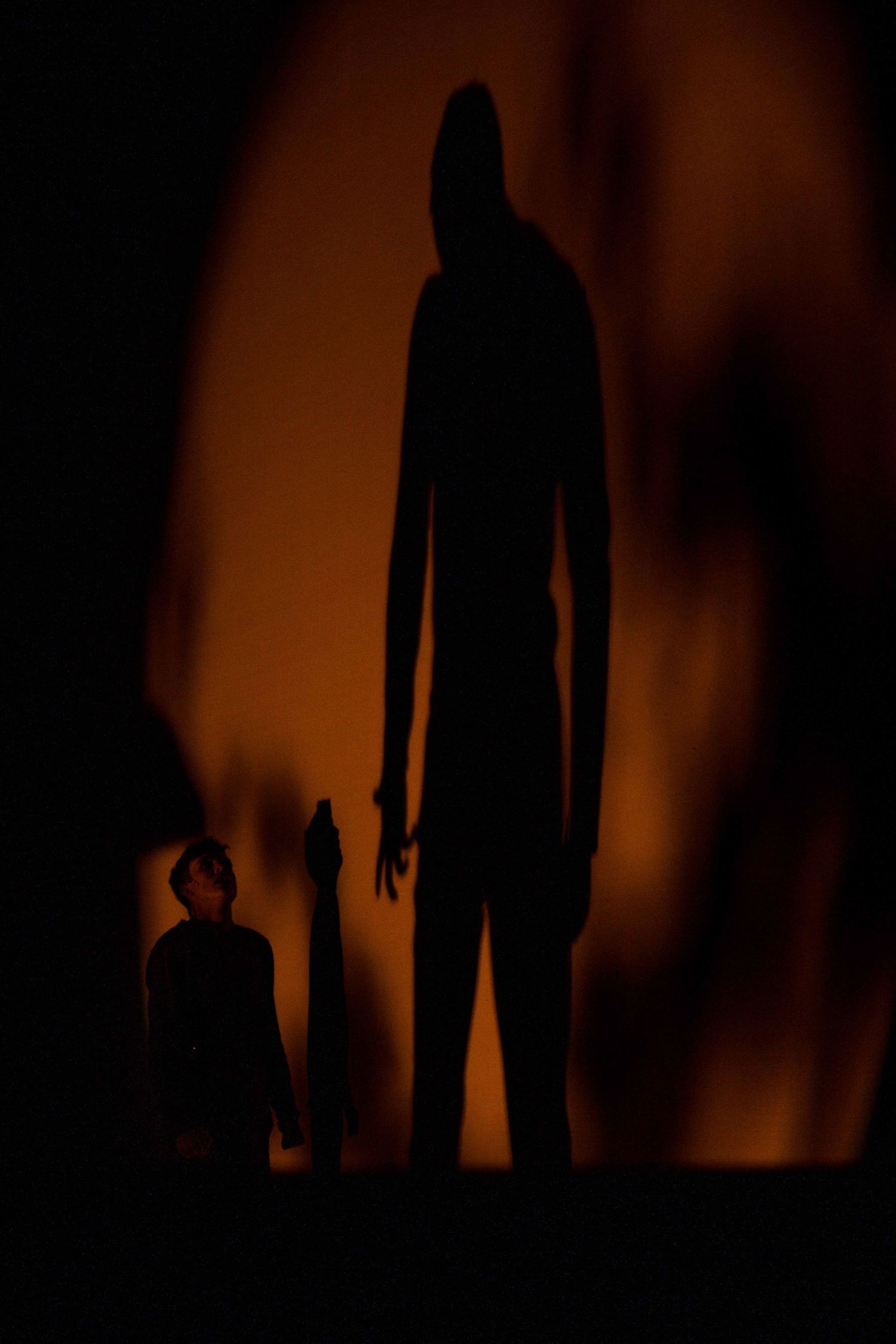 Dark silhouettes of people standing against an orange-lit background creating dramatic shadows.